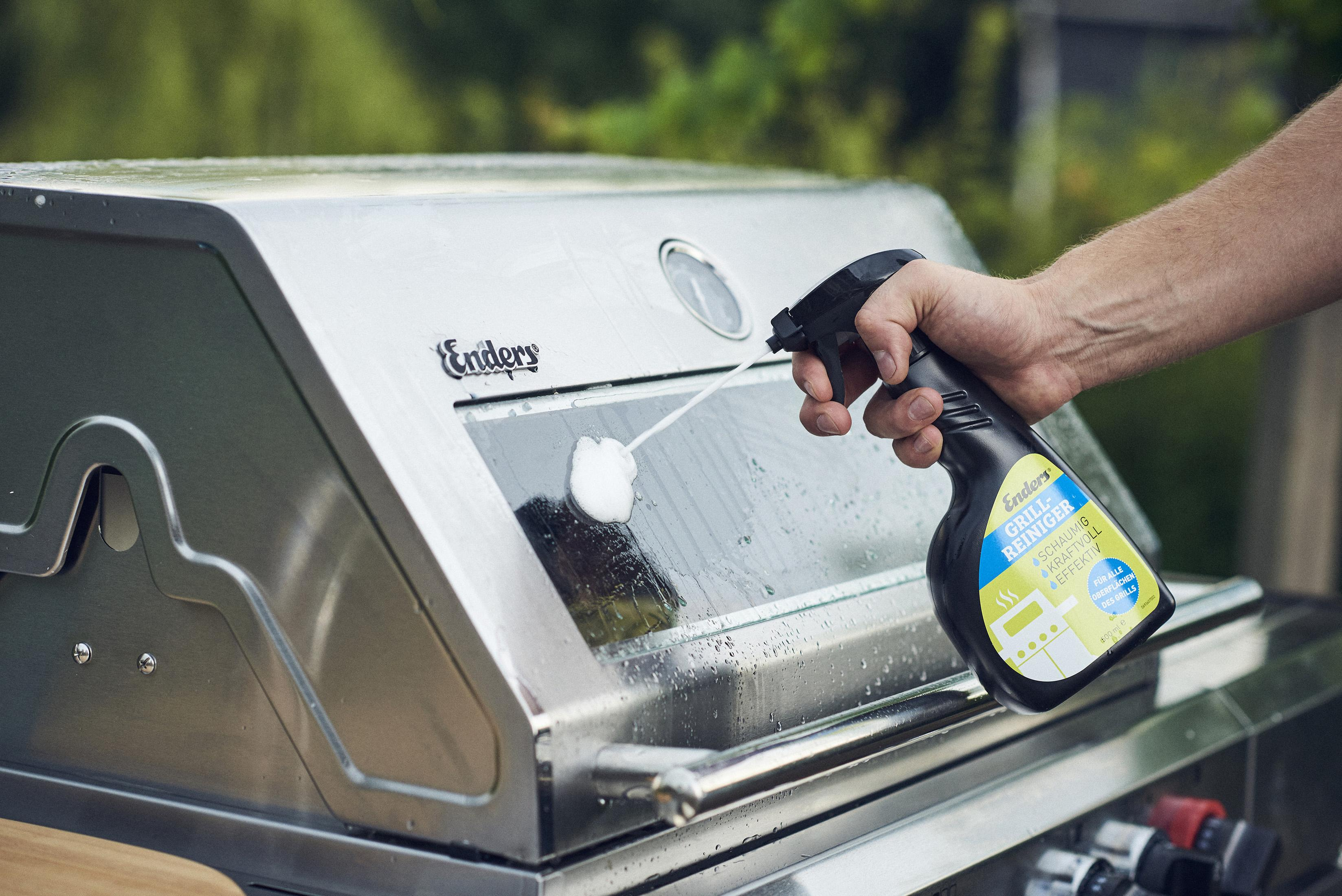 Person reinigt einen Grill mit Spray und Tuch. Enders Grill sichtbar.