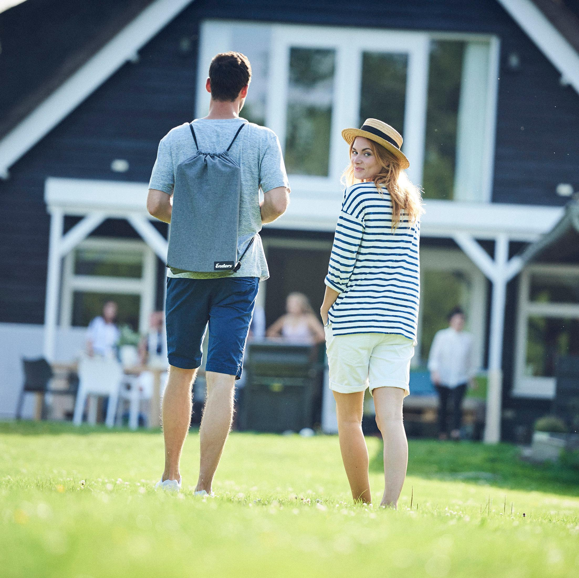 Ein Mann und eine Frau gehen über Gras. Die Frau schaut in die Kamera. Ein Haus ist im Hintergrund.