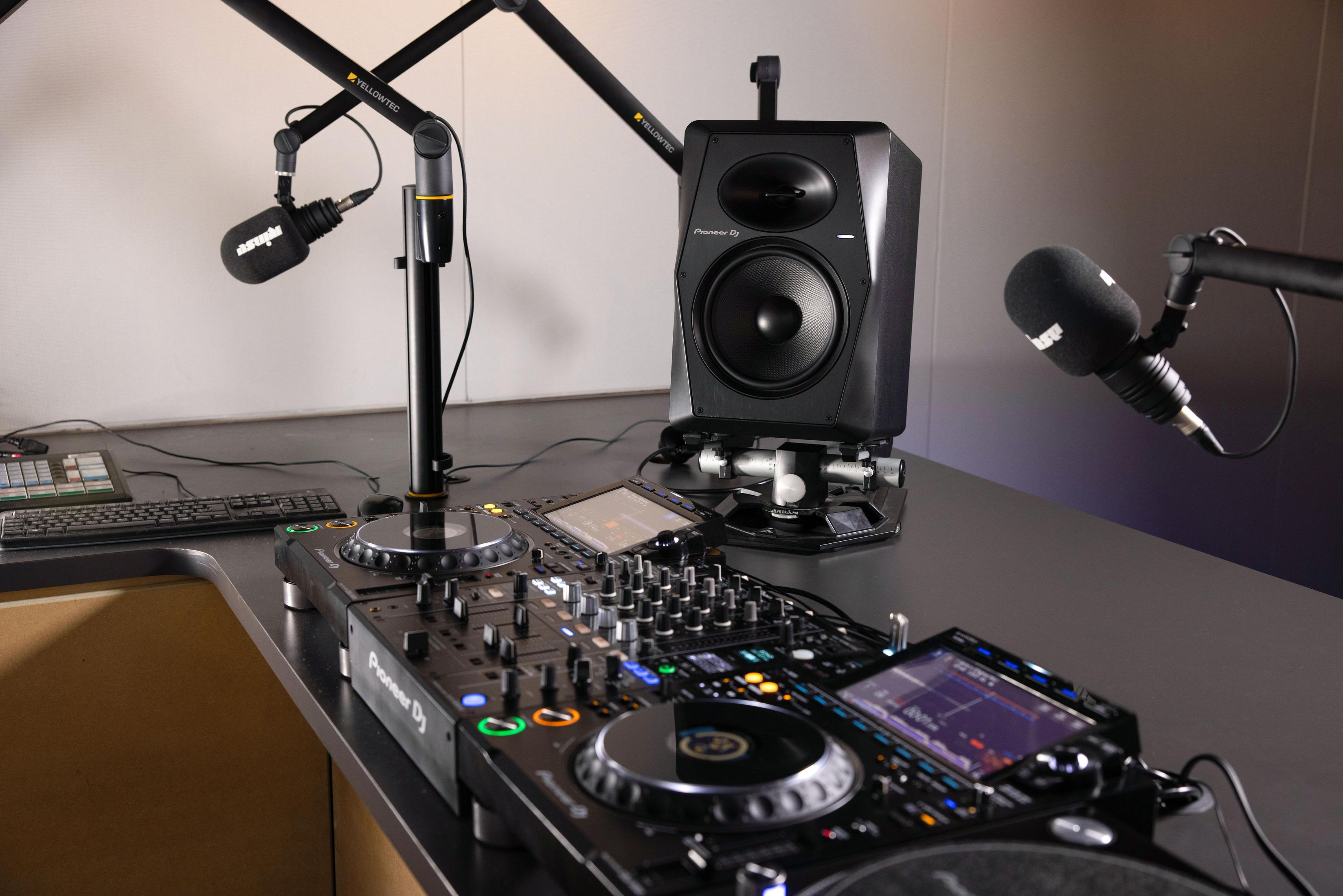 Configuración de DJ en un escritorio. Hay dos micrófonos y un altavoz. El equipo de DJ es visible.