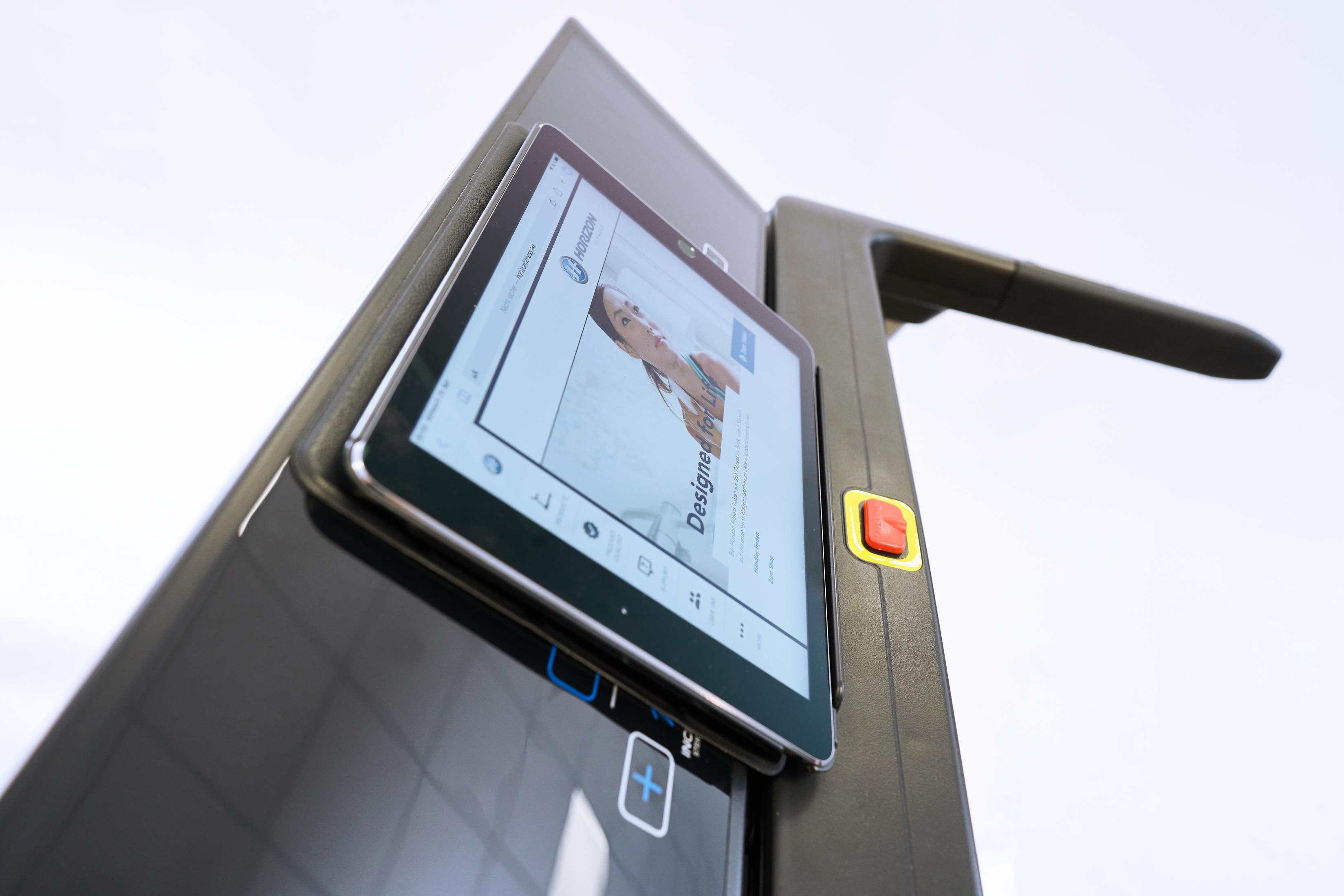Tablet collegato a un tapis roulant nero. Lo schermo del tablet mostra una pagina web con la parola 'Designer'.