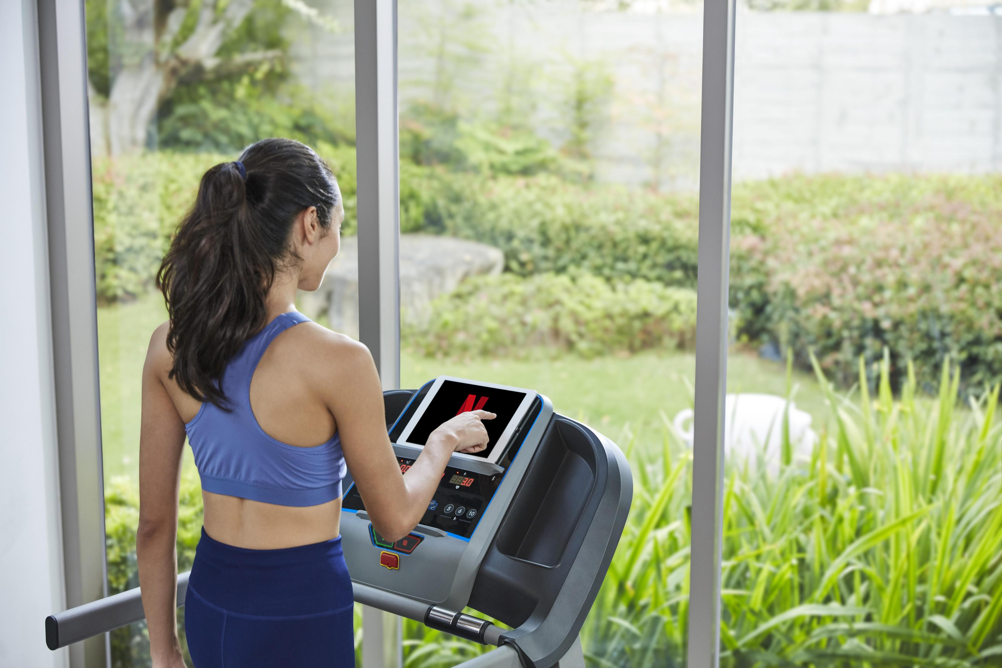 Donna su tapis roulant, tocca lo schermo del tablet. In palestra domestica.