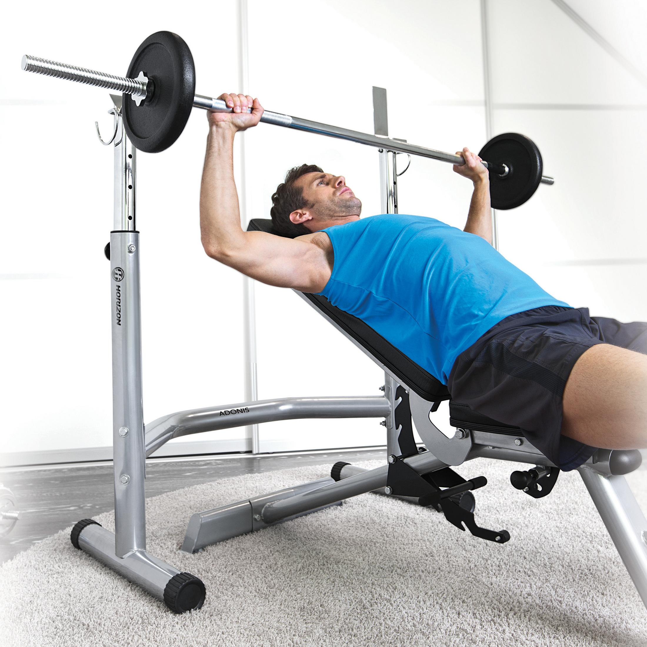 Mężczyzna podnosi ciężary na ławce do wyciskania z hantlami w domowej siłowni.