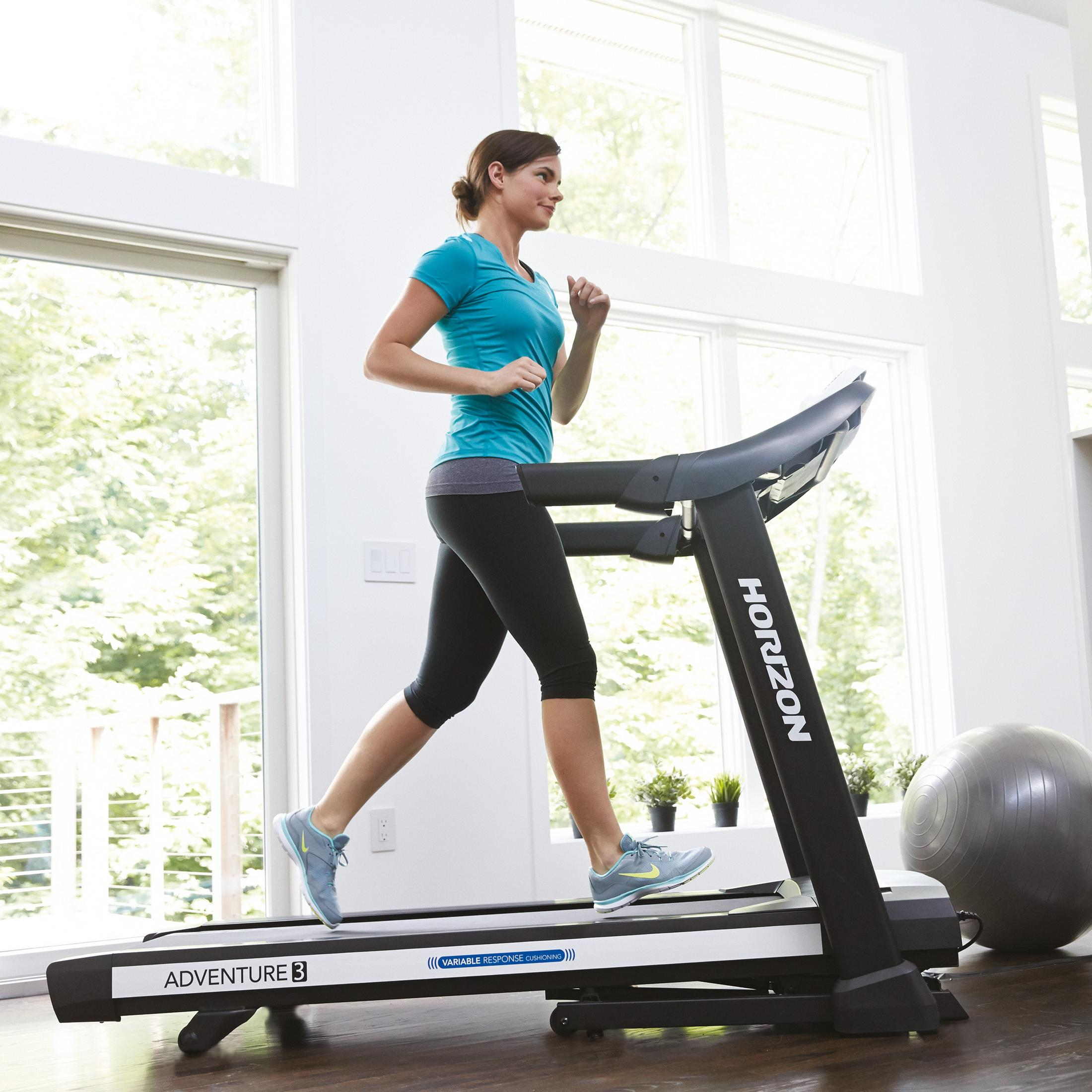 Woman running on treadmill. She is wearing athletic clothes. Bright, sunny room.