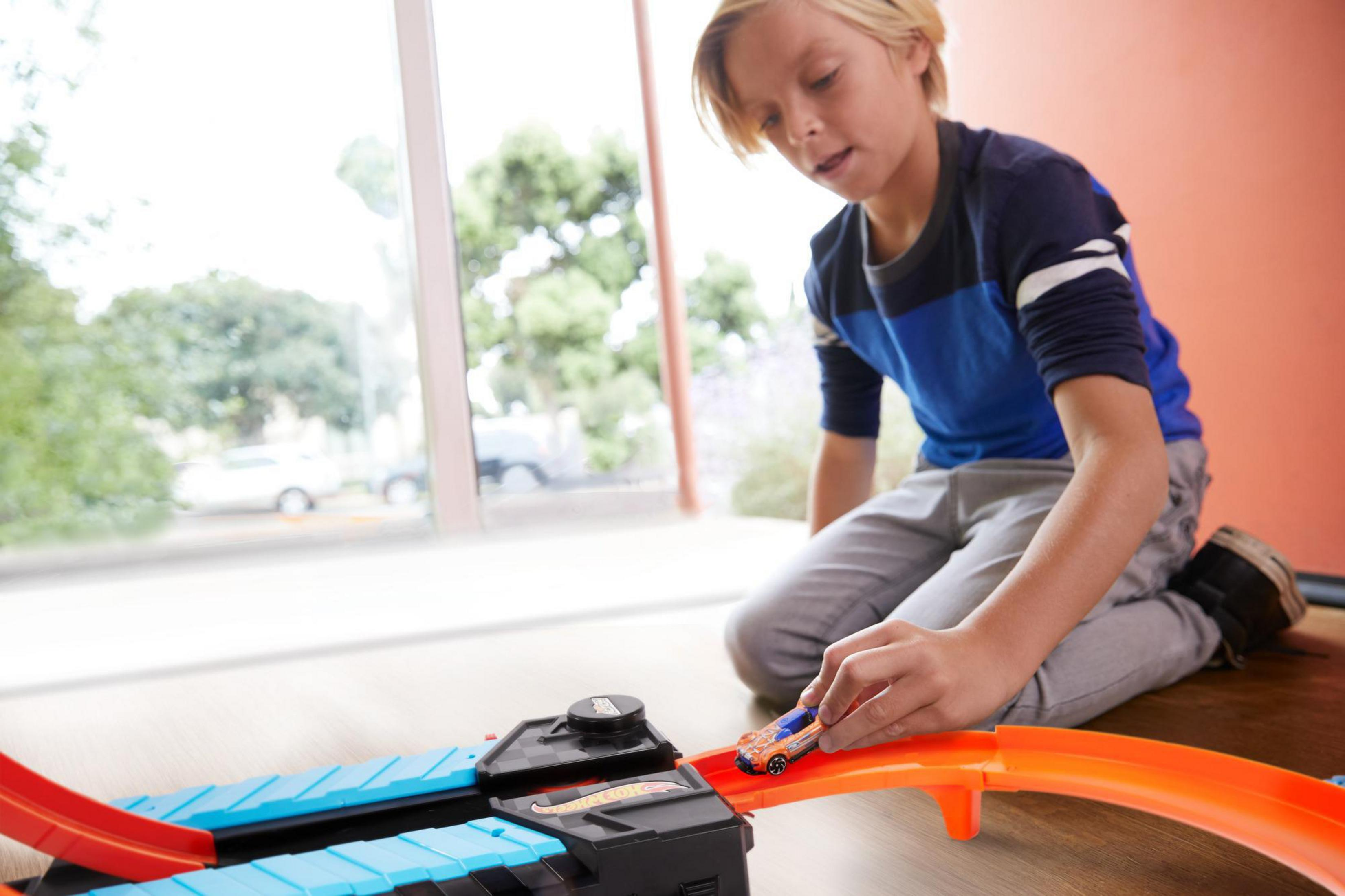 Chłopiec bawiący się zabawką na torze Hot Wheels. Samochód jest niebiesko-pomarańczowy.