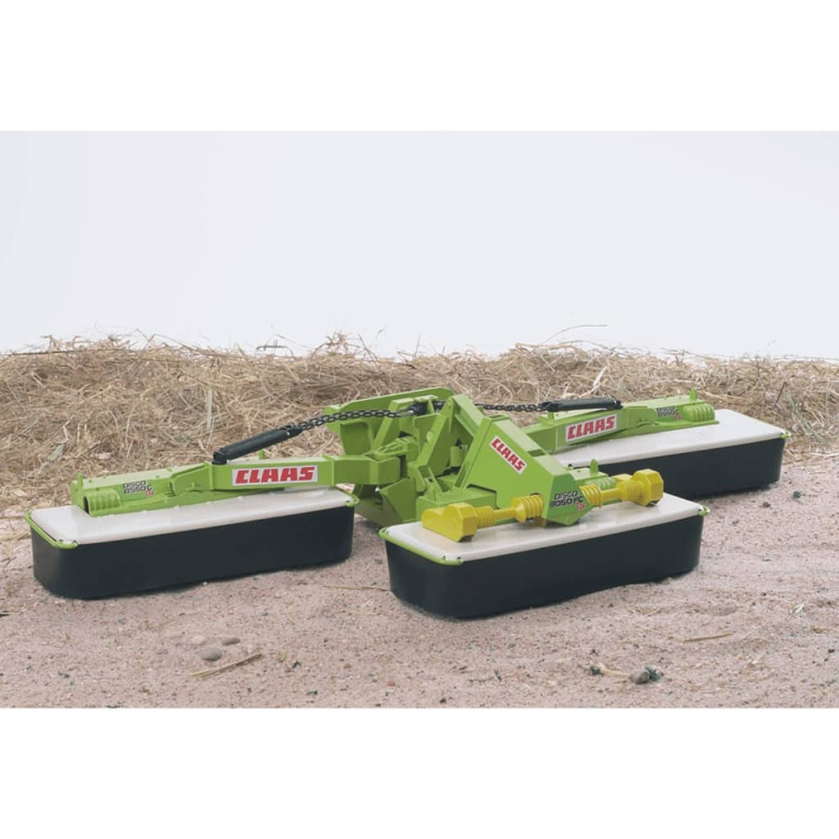 Zielona zabawka do koszenia CLAAS z trzema pokładami tnącymi na podłożu pokrytym słomą.