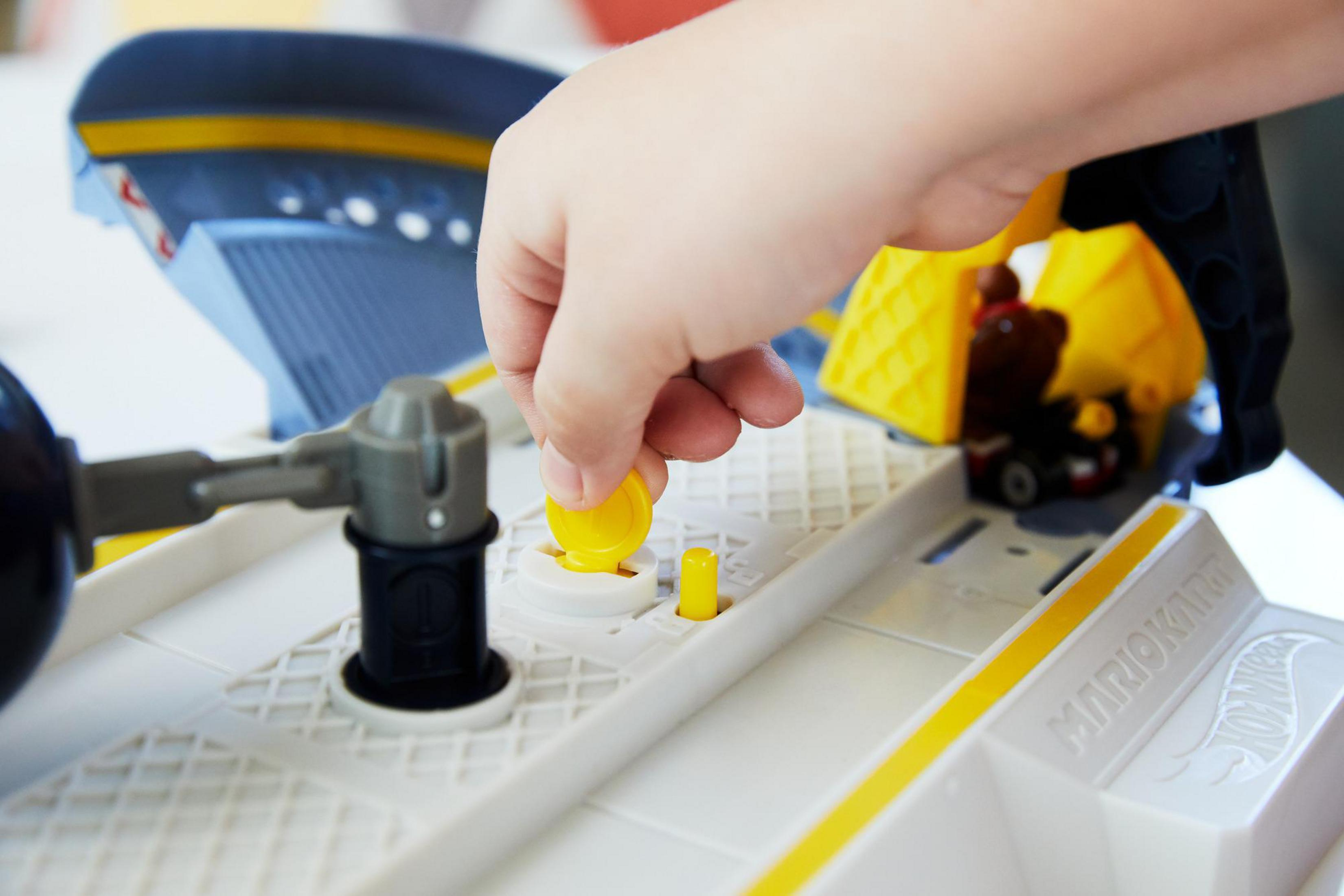 Dłoń dziecka umieszczająca monetę na torze Hot Wheels Mario Kart. Obecne kolory żółty i szary.