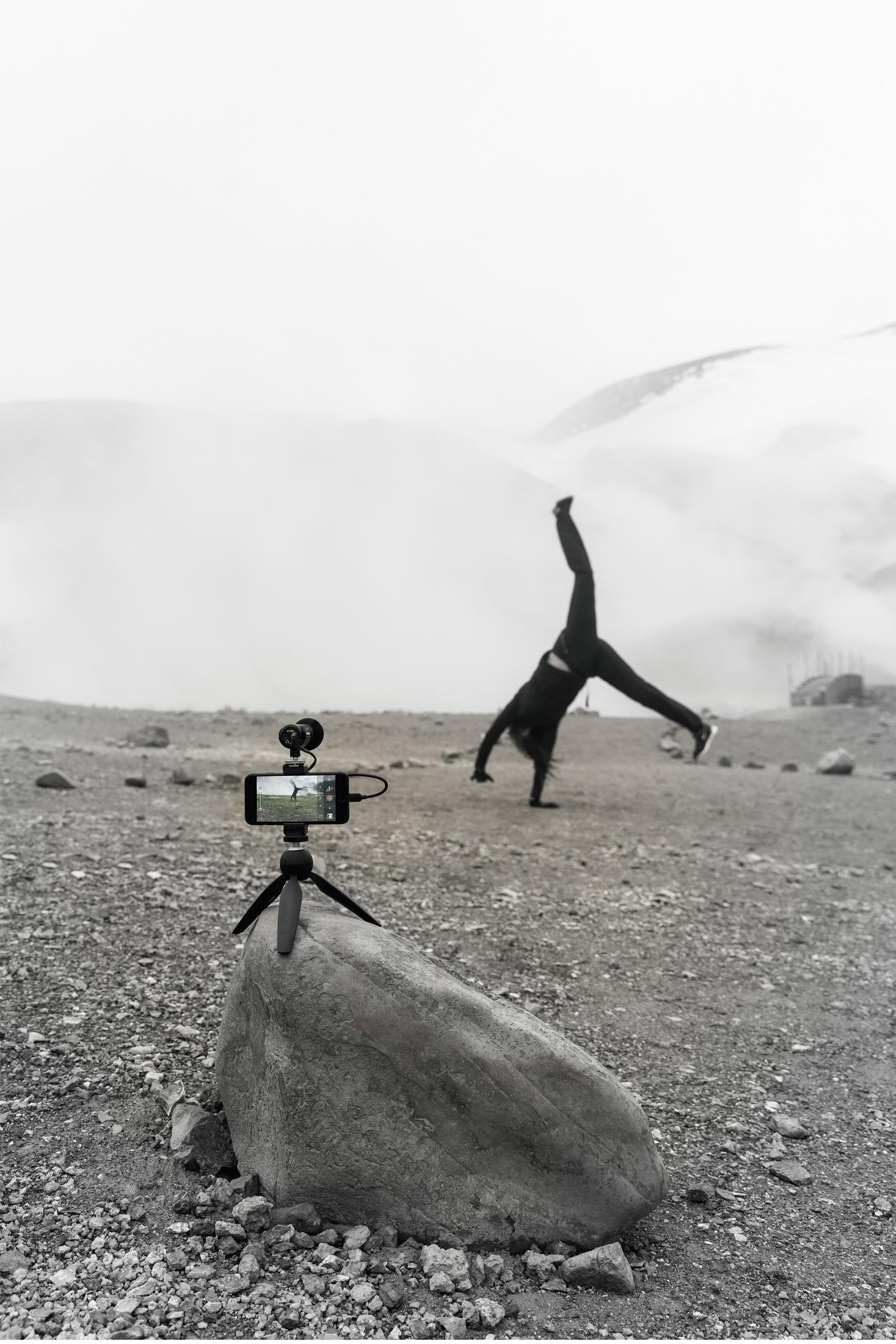 Person macht Handstandüberschlag, gefilmt vom Handy auf Stativ. Felsige Landschaft im Hintergrund.