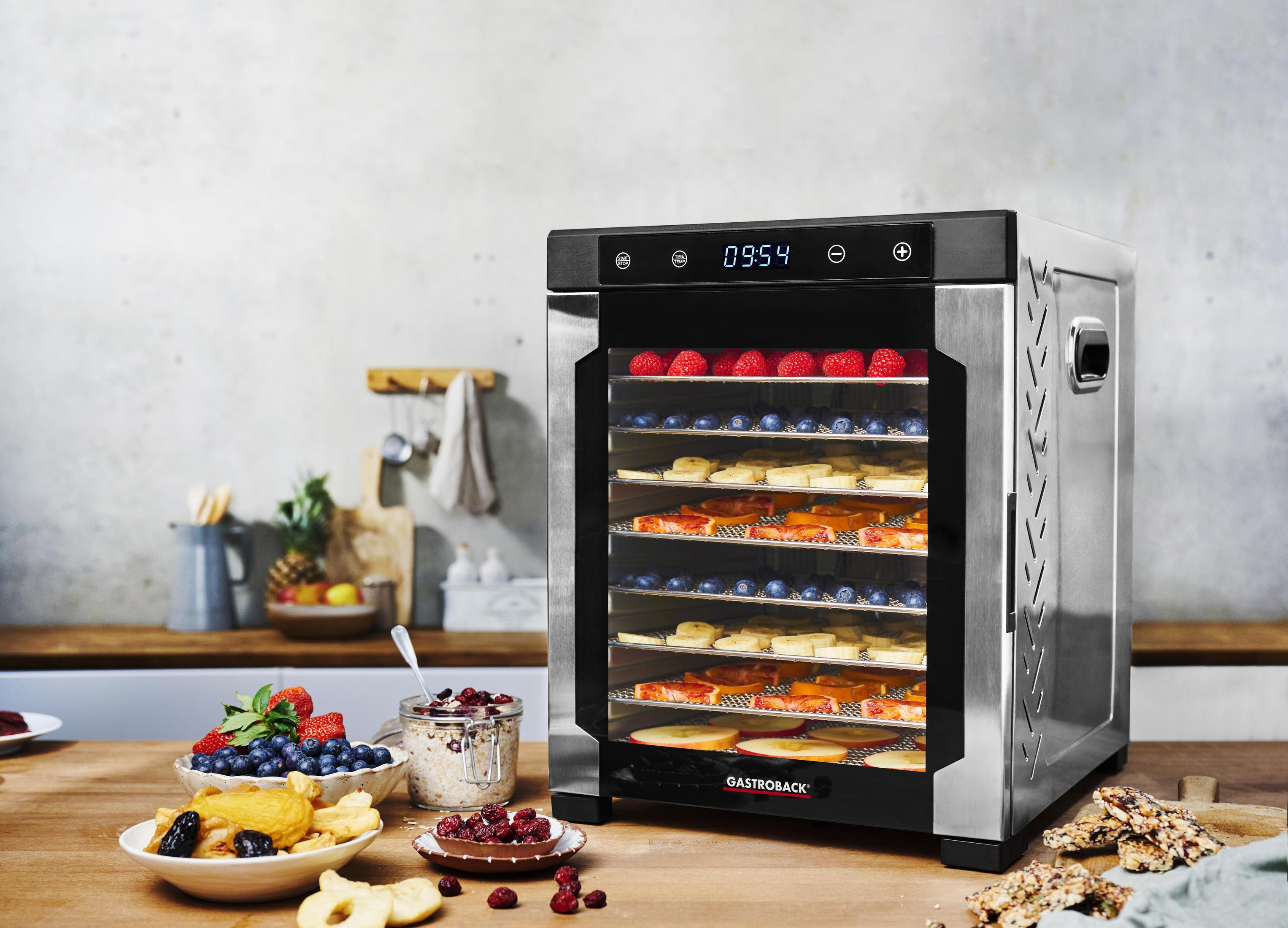 Essiccatore alimentare in acciaio inox con frutta sui vassoi. Ingredienti su tavolo di legno.