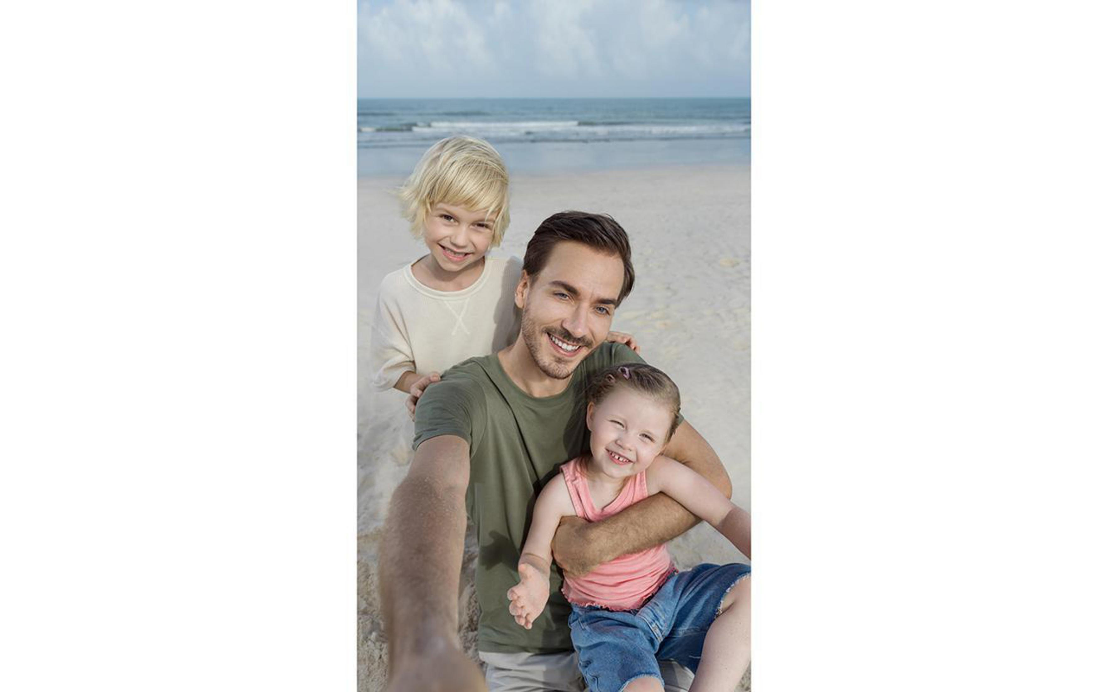 Vater und zwei Kinder lächeln für ein Selfie am Strand, sonniger Tag.