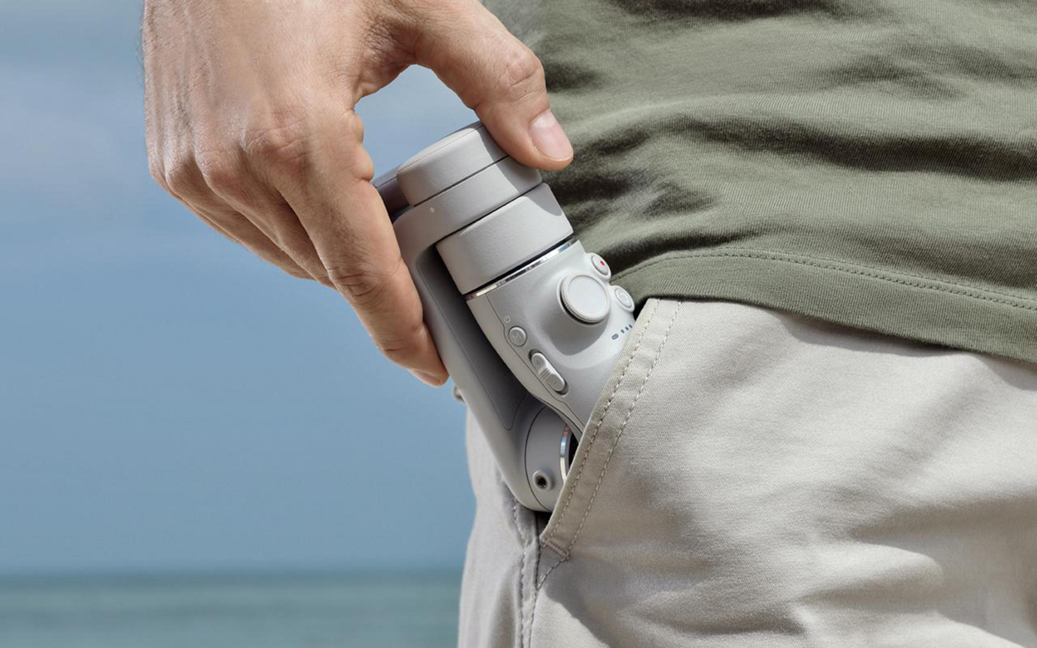 Hand, die ein weißes und graues Gimbal hält, teilweise in eine Khakitasche gesteckt.