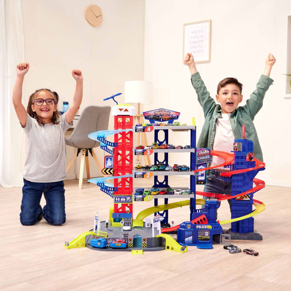 Zwei Kinder feiern in der Nähe einer Spielzeuggarage mit Spielzeugautos. Die Garage ist mehrstöckig.