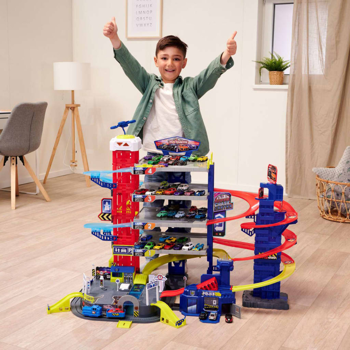 Ein Kind steht vor einer Spielzeug-Parkgarage mit Autos. Das Kind zeigt den Daumen hoch.