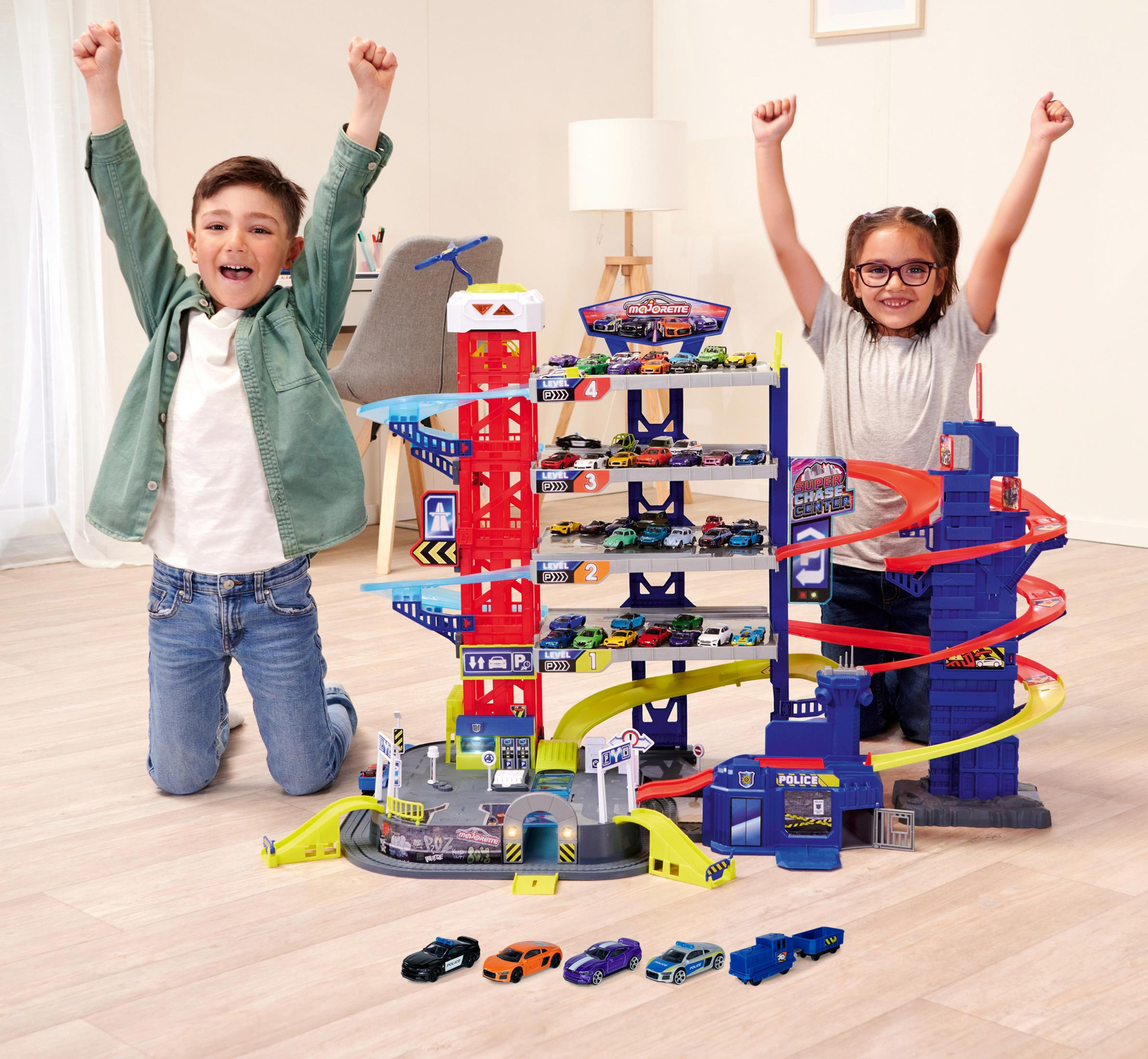 Zwei Kinder jubeln mit erhobenen Armen vor einer Spielzeug-Garage voller Autos.