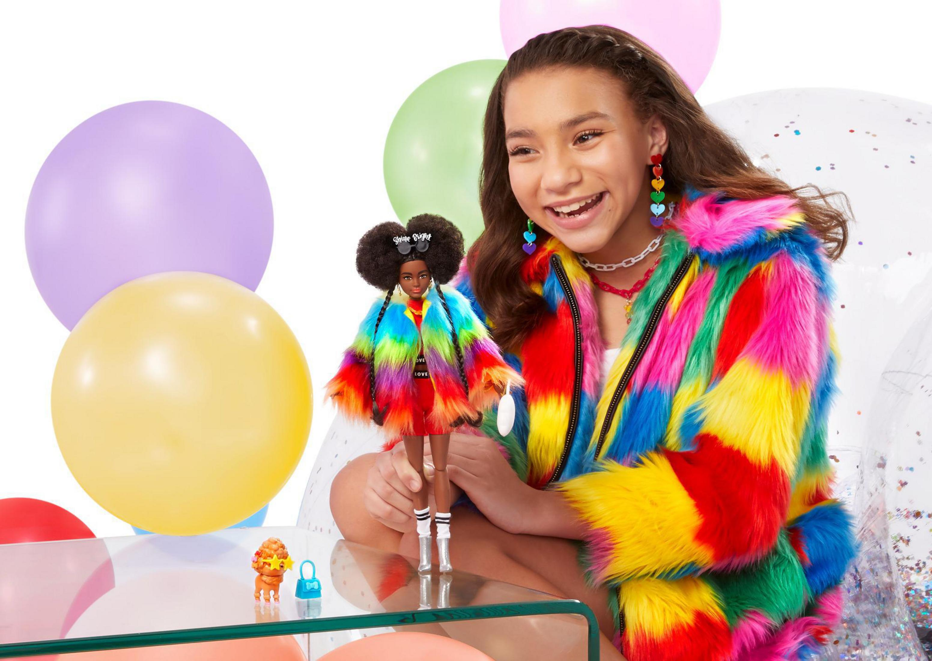 Ein Mädchen mit einer Puppe und Luftballons. Das Mädchen und die Puppe tragen bunte Kleidung.
