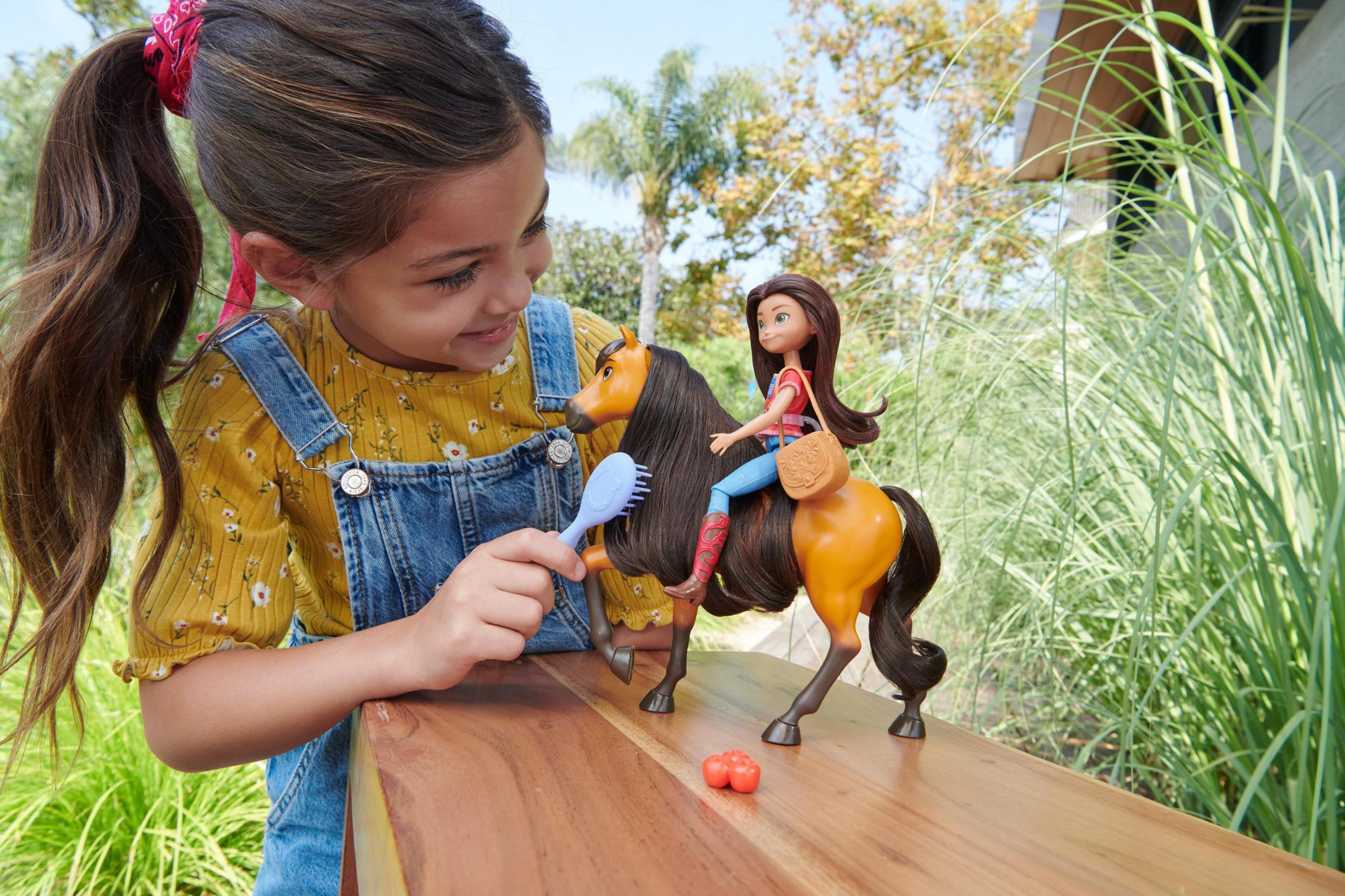 Dziewczynka z koniem zabawką i lalką na drewnianej powierzchni, bawiąca się szczotką.