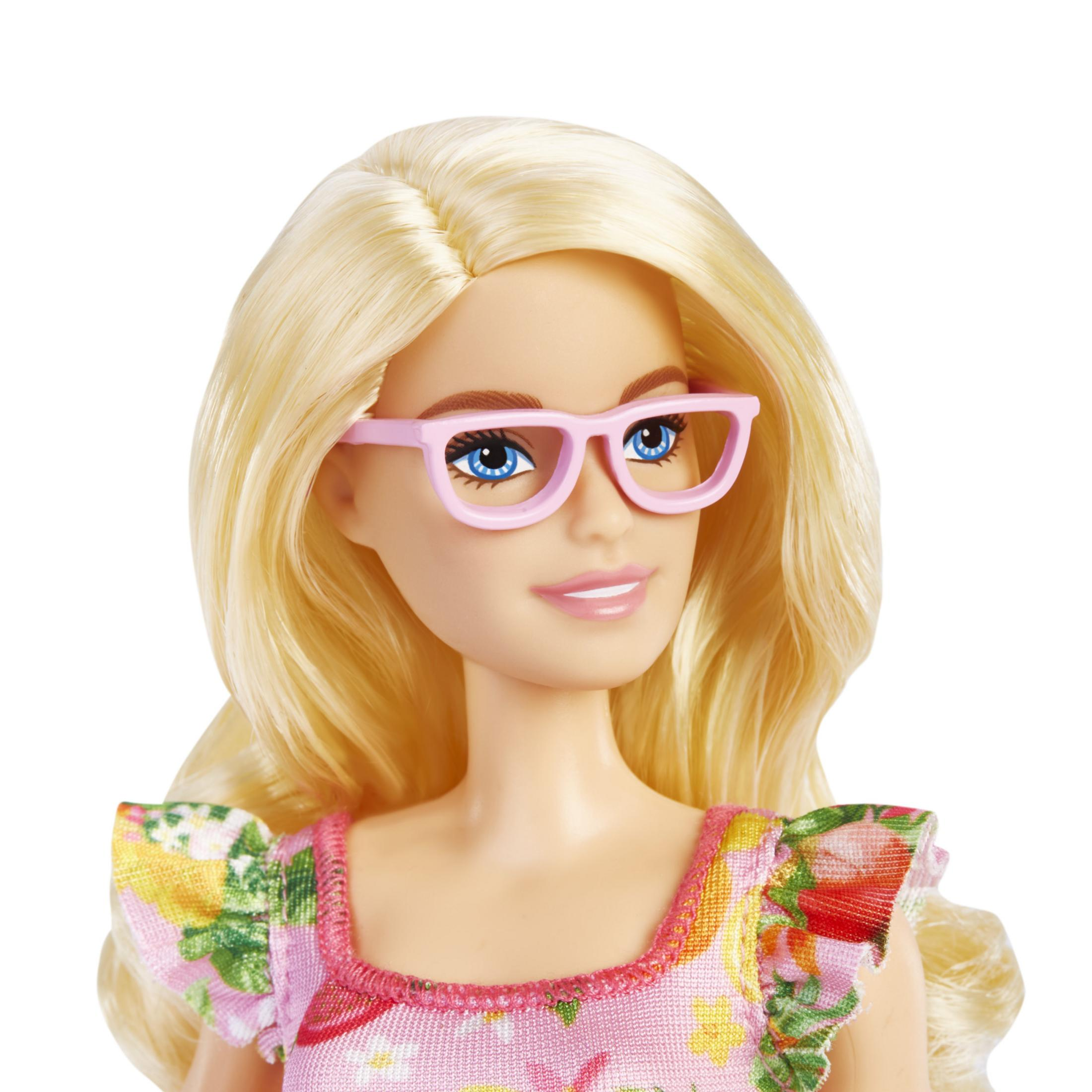 Blond Barbie w różowych okularach i kwiecistej sukience, uśmiecha się do kamery.