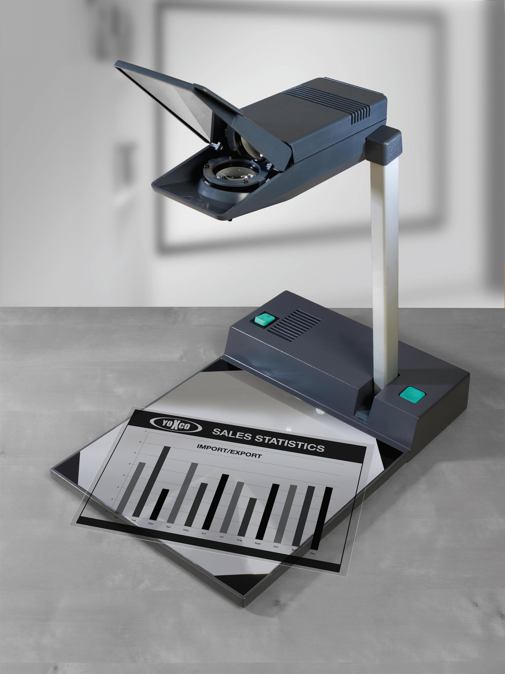 Rzutnik wyświetlający wykres statystyk sprzedaży na szarej powierzchni, z białą ścianą.