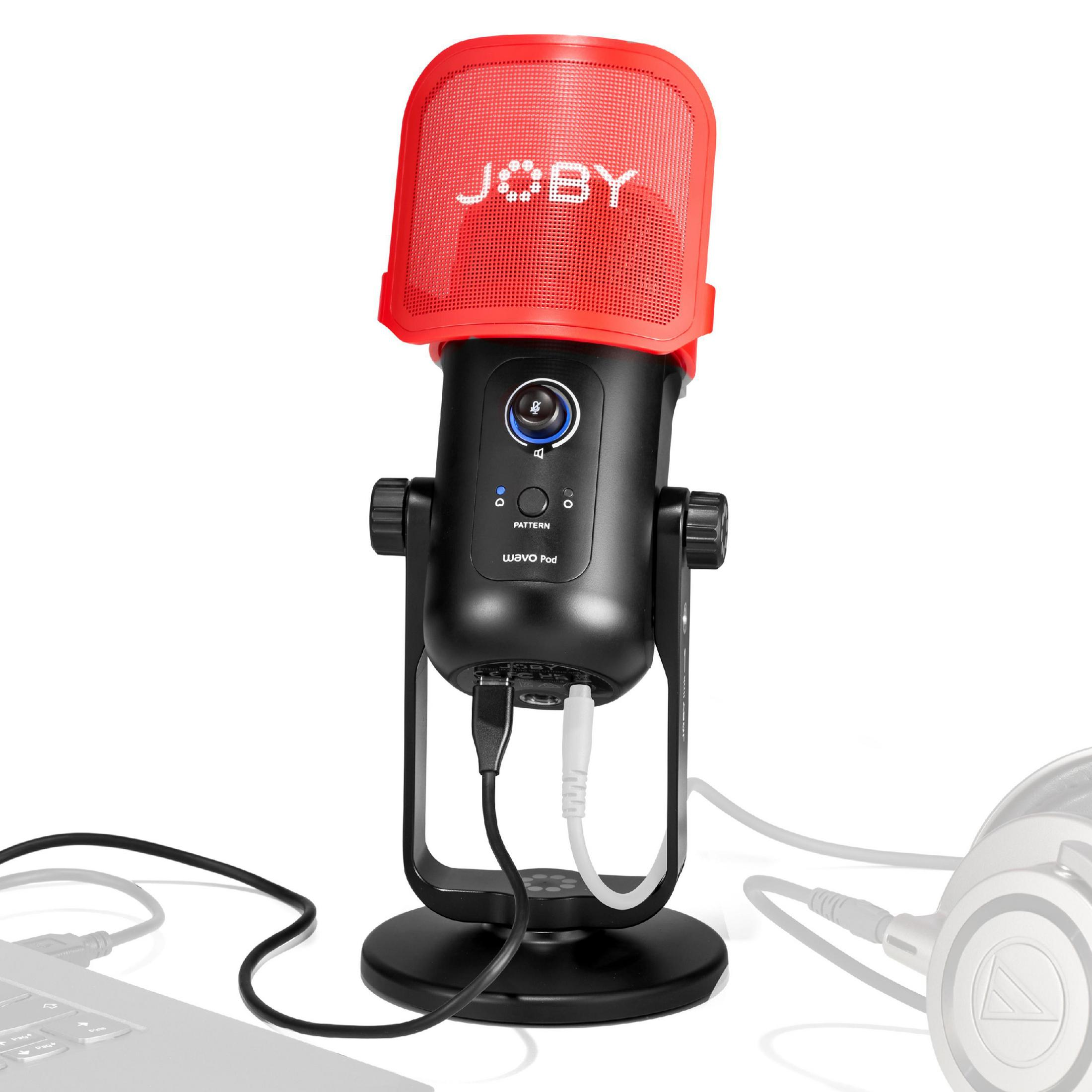 Micrófono negro con malla roja, sobre un soporte, con cables y auriculares a un lado.
