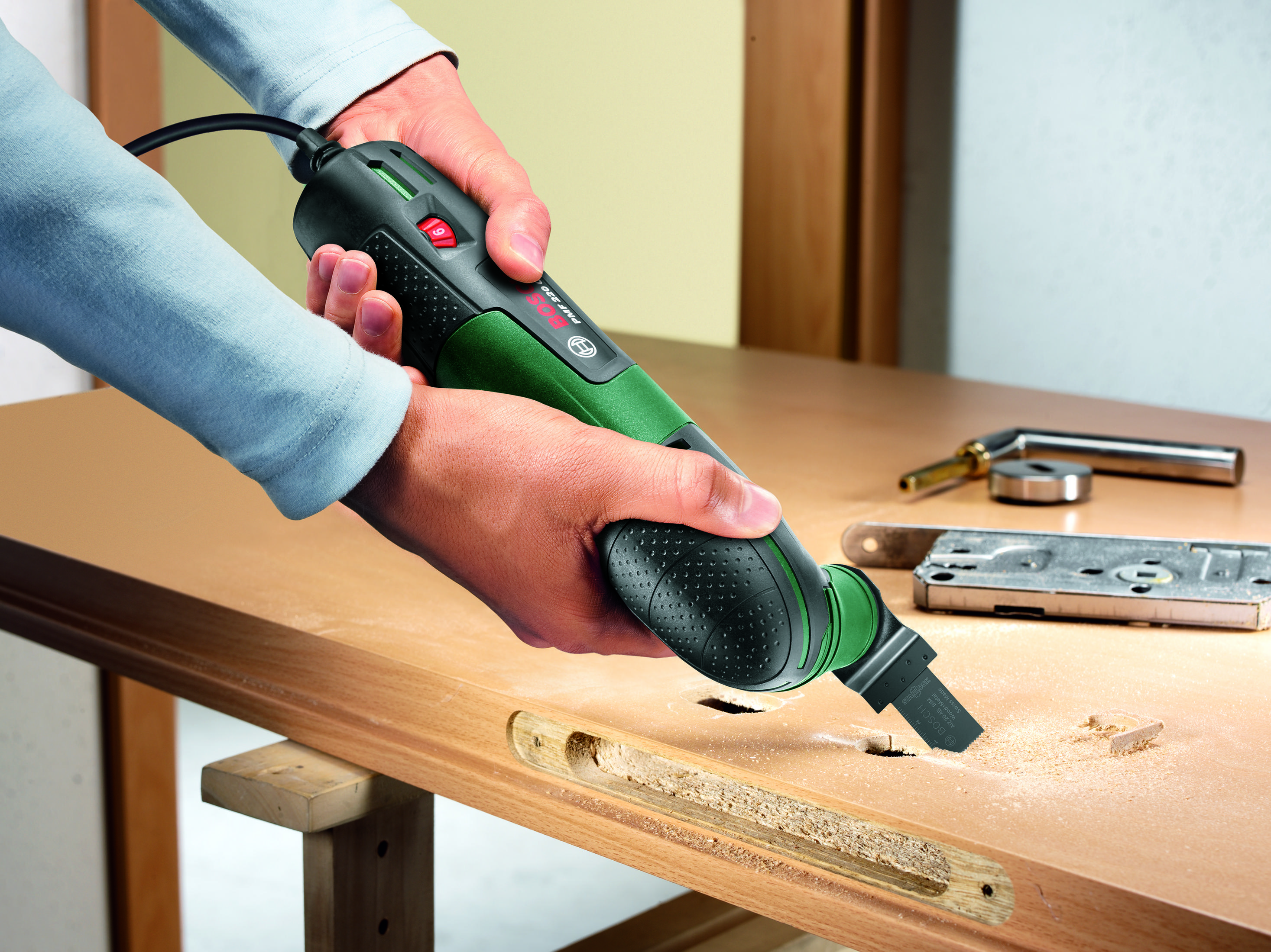 Osoba używająca narzędzia wielofunkcyjnego Bosch do cięcia drewnianych drzwi, obecne wióry.