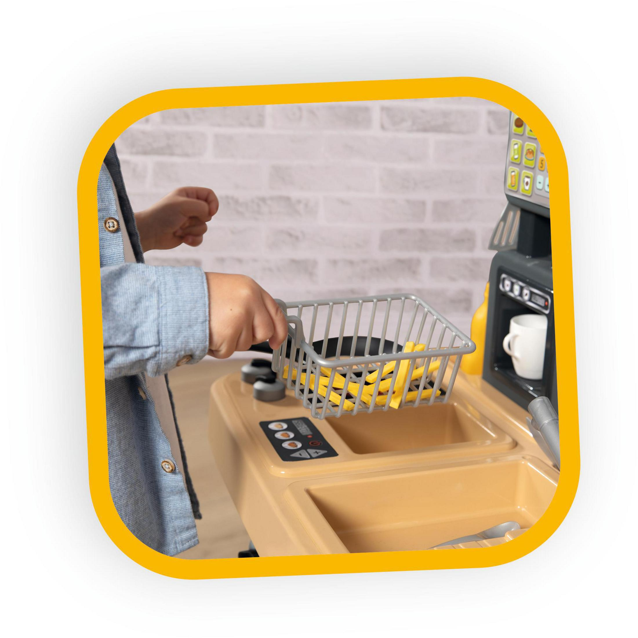 Ręce dziecka trzymają kosz frytek nad zlewozmywakiem zabawki. Żółta ramka.