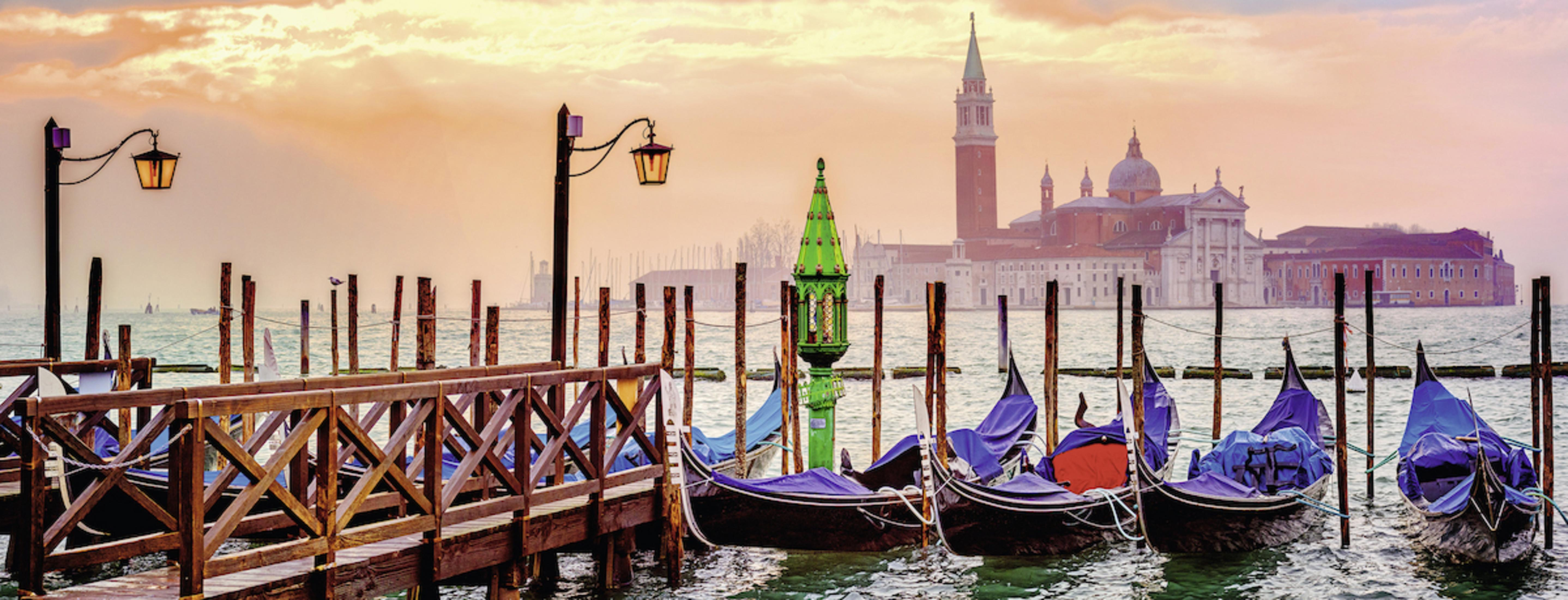 Panoramablick auf Venedig. Gondeln angedockt, Gebäude im Hintergrund, Sonnenaufgangs-/Sonnenuntergangsfarben.