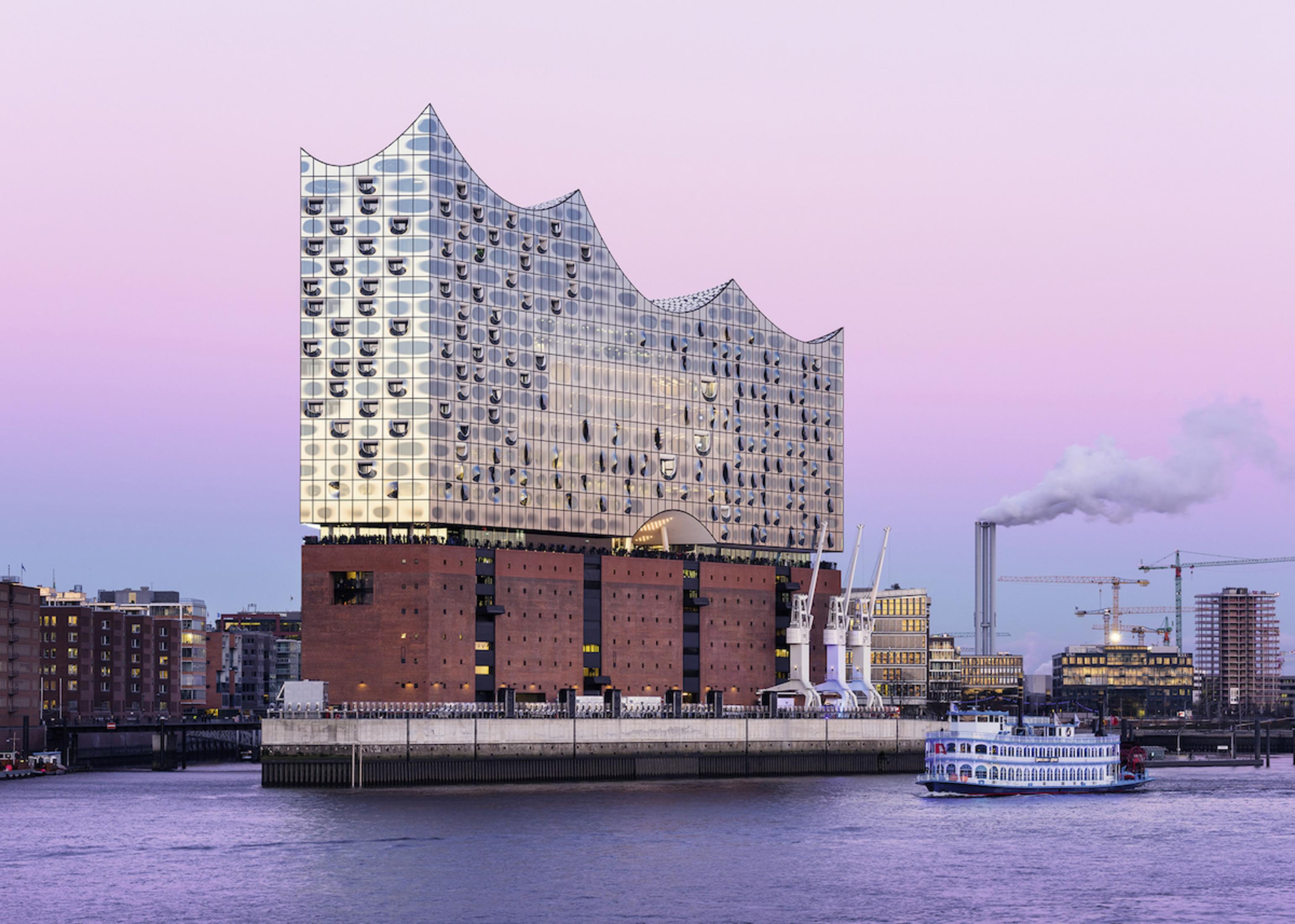 Elbphilharmonie-Gebäude mit Wasser davor. Es ist ein modernes Gebäude mit Glas und einem Boot davor.