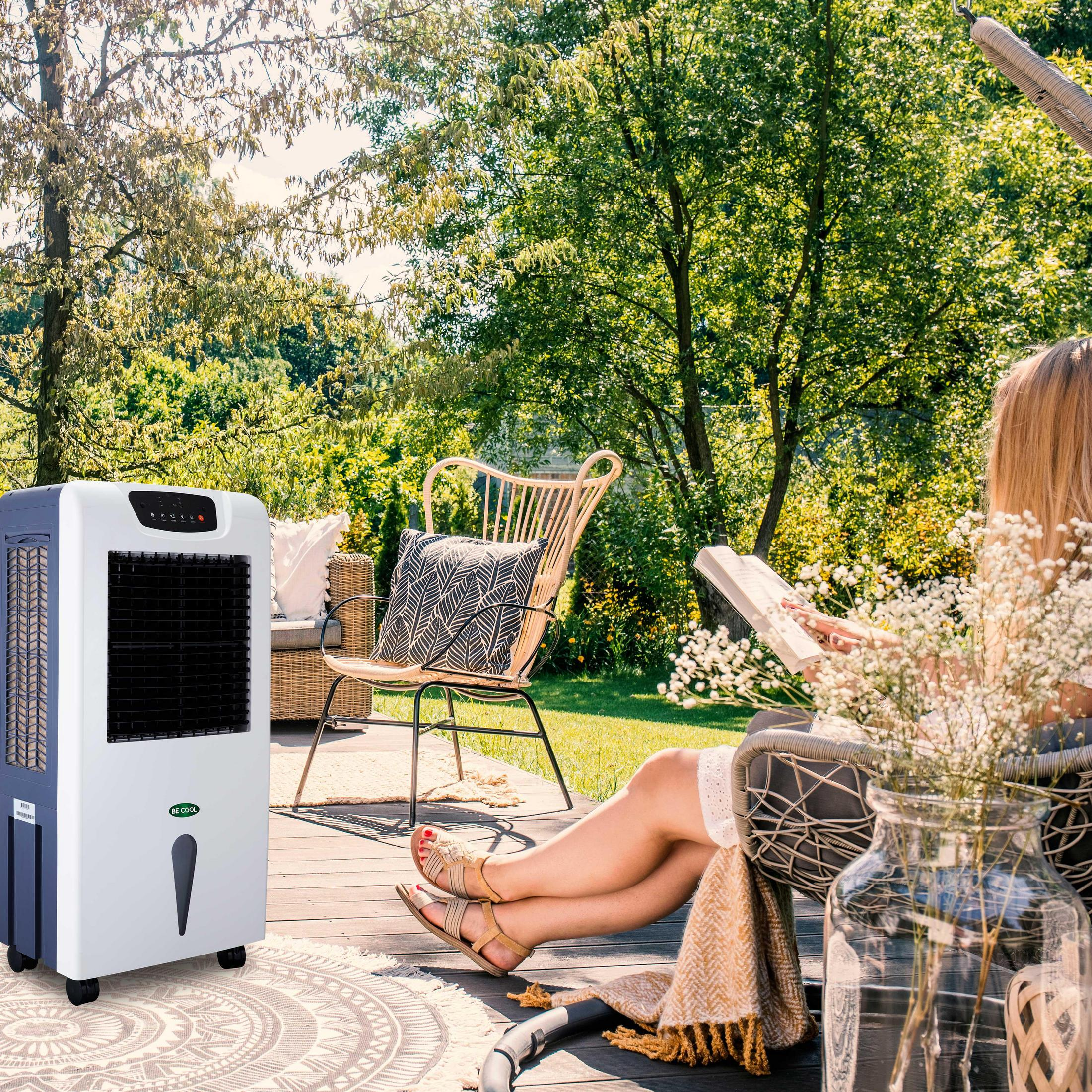 Eine Frau liest im Garten, im Hintergrund ein Kühler.