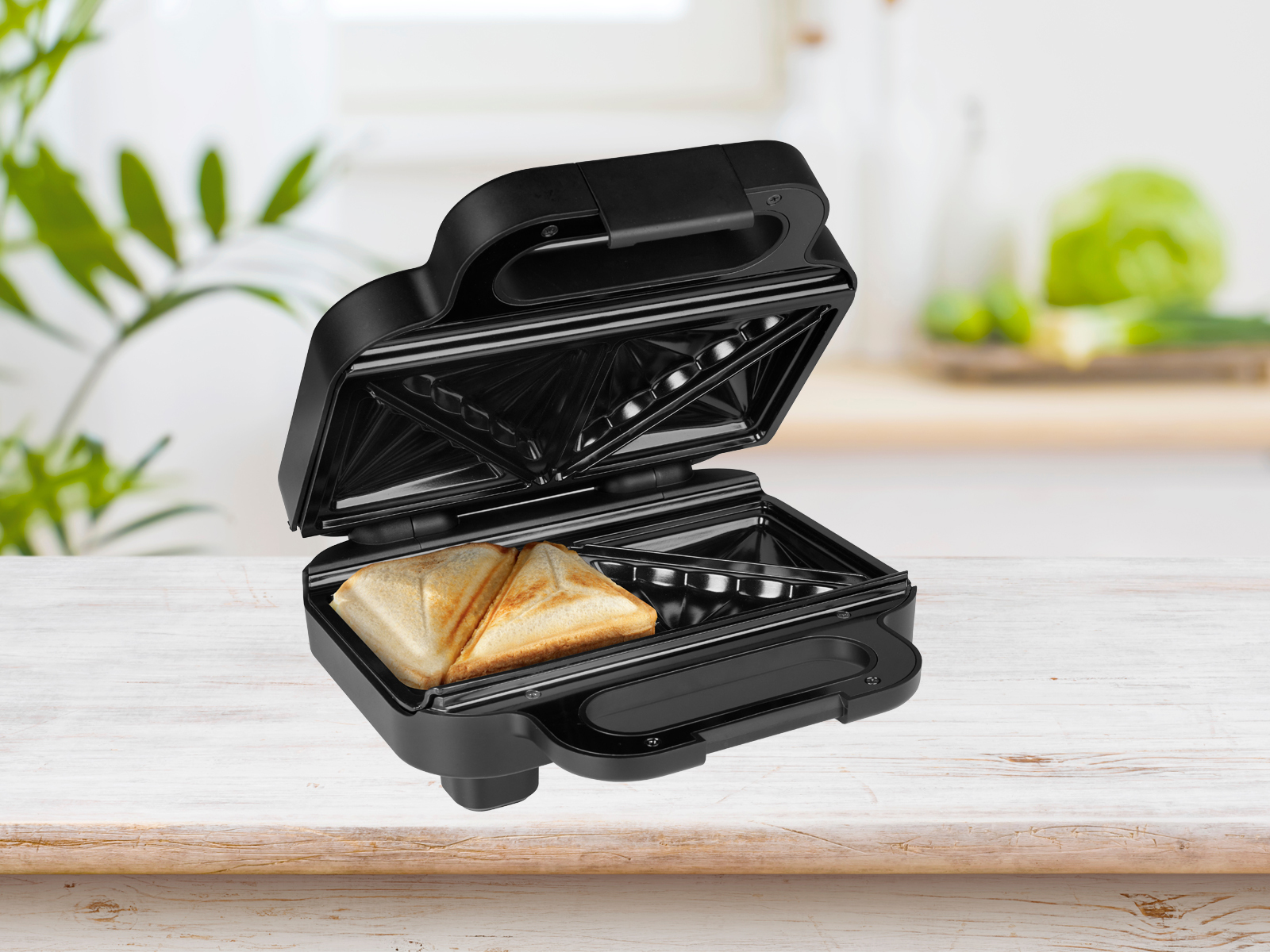 Sandwich maker nero con due toast all'interno, aperto su una superficie di legno.