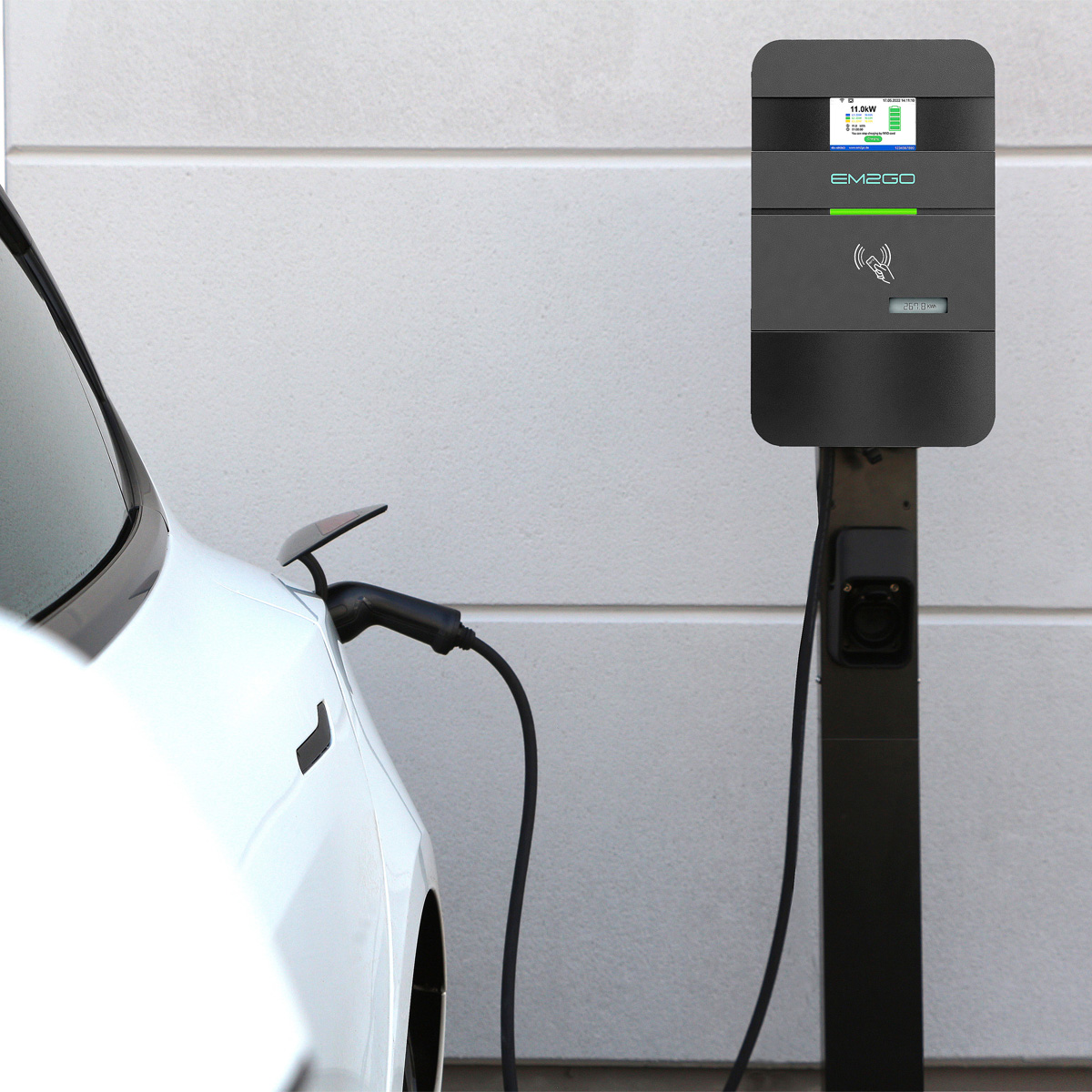 Weißes Elektroauto, das an einer EM2GO-Ladestation geladen wird. Die Station ist schwarz und hat einen Bildschirm.