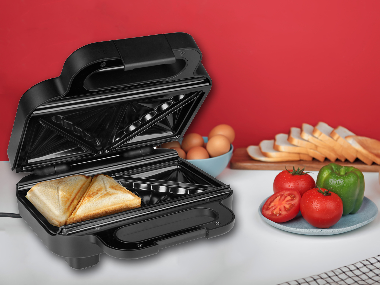 Ein schwarzer Sandwichmaker mit zwei Sandwiches auf dem Grill und Zutaten daneben.