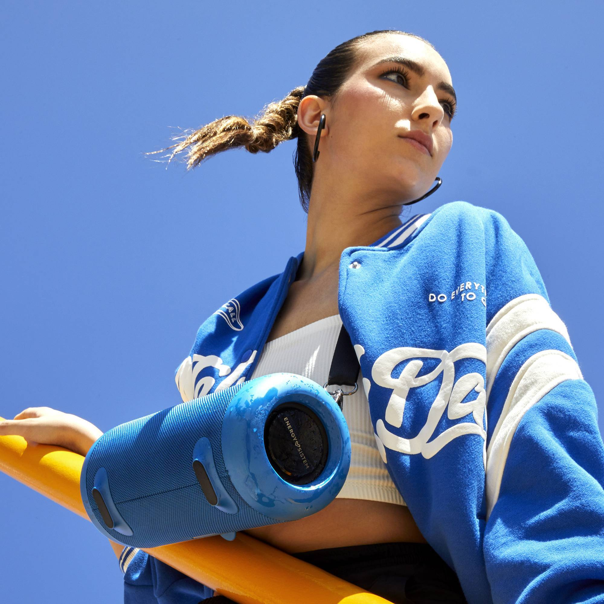 Una donna con un altoparlante blu su un palo giallo, cielo blu sullo sfondo.
