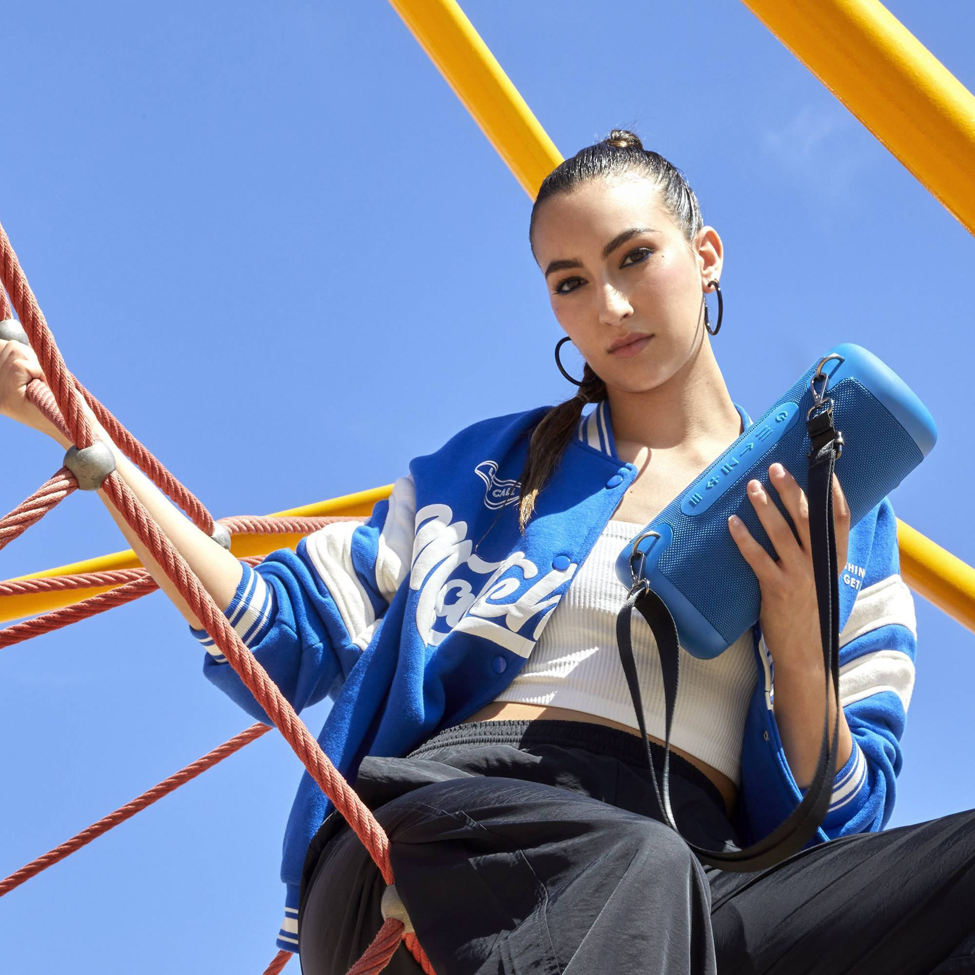 Donna che tiene un altoparlante blu in un parco giochi, indossa una giacca blu e pantaloni neri.