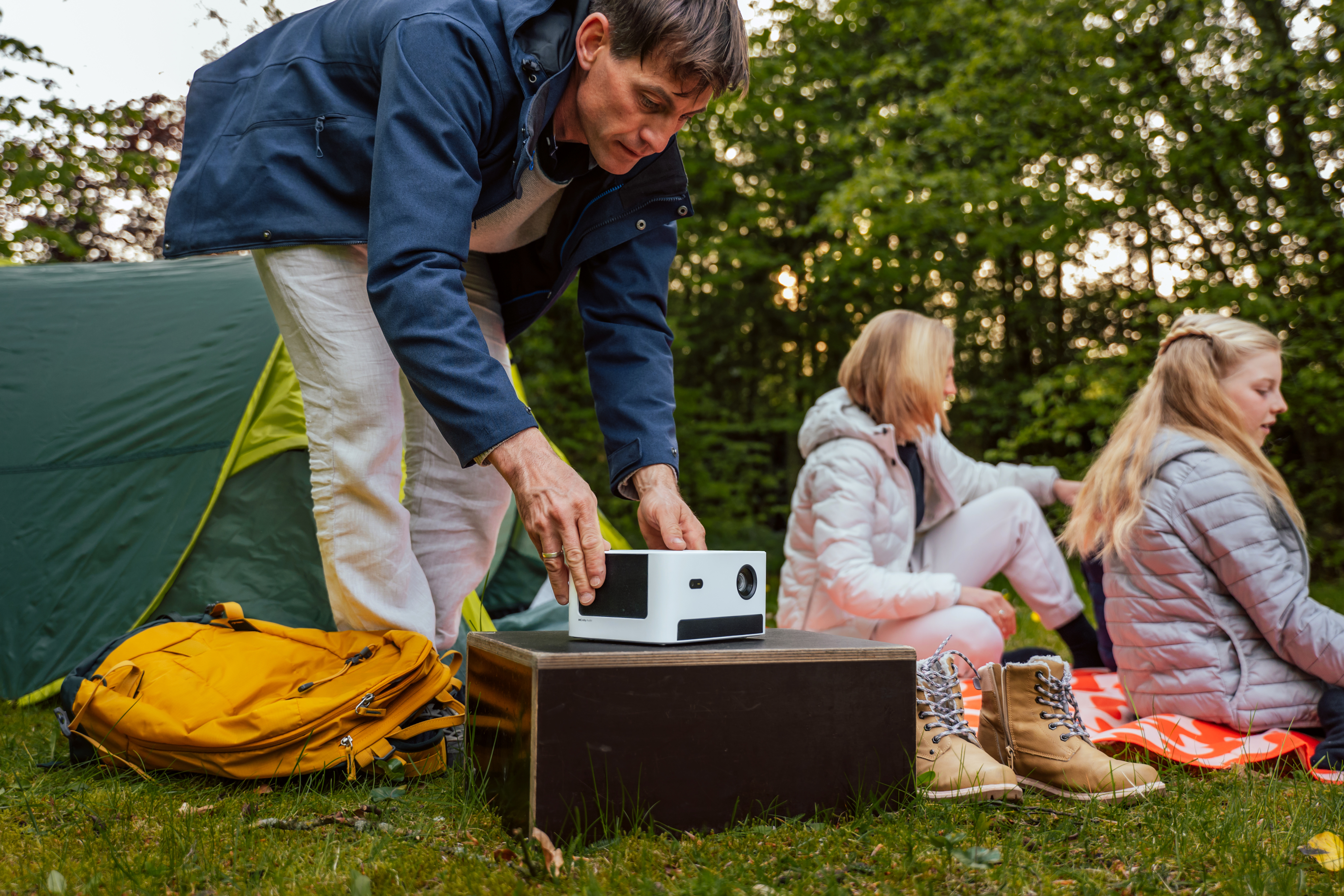 Rodzina ustawia projektor na zewnątrz. Mężczyzna umieszcza projektor na pudełku.