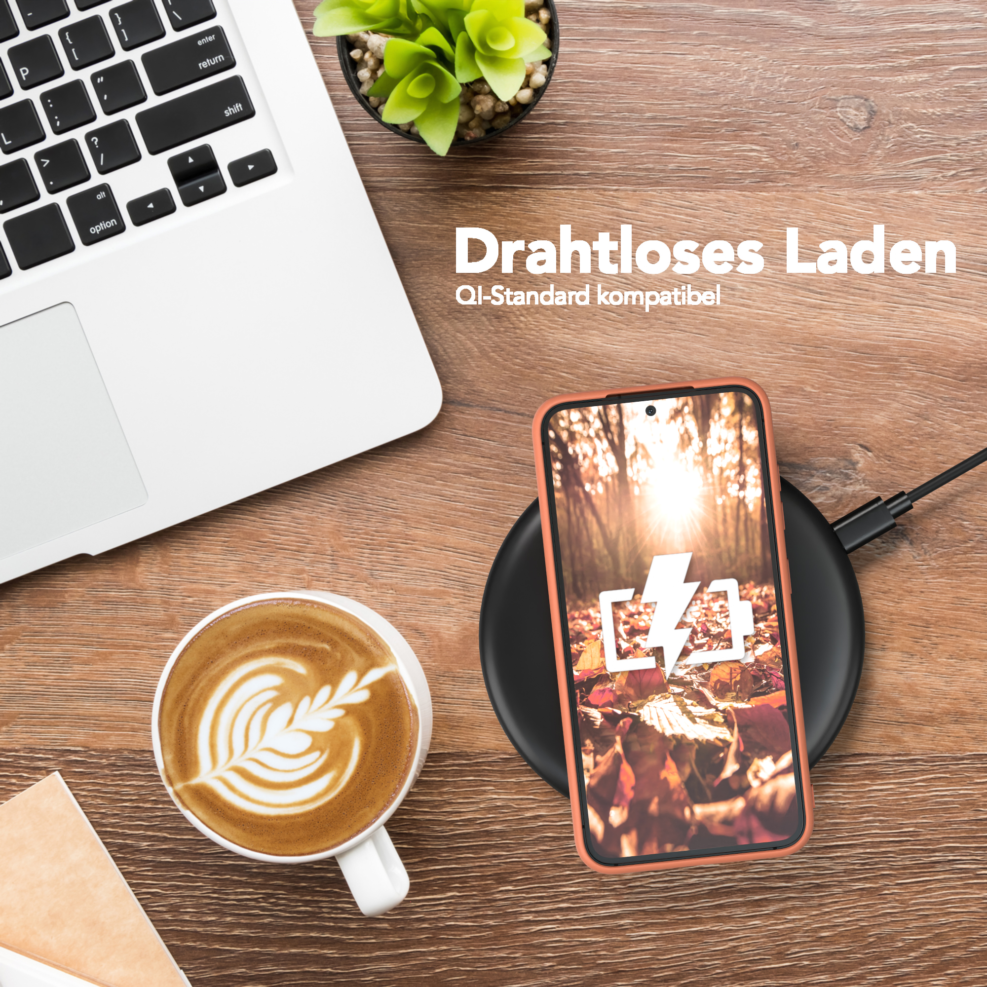 Telefon wird drahtlos auf einem Pad aufgeladen, neben einem Laptop und einer Kaffeetasse mit Latte Art.