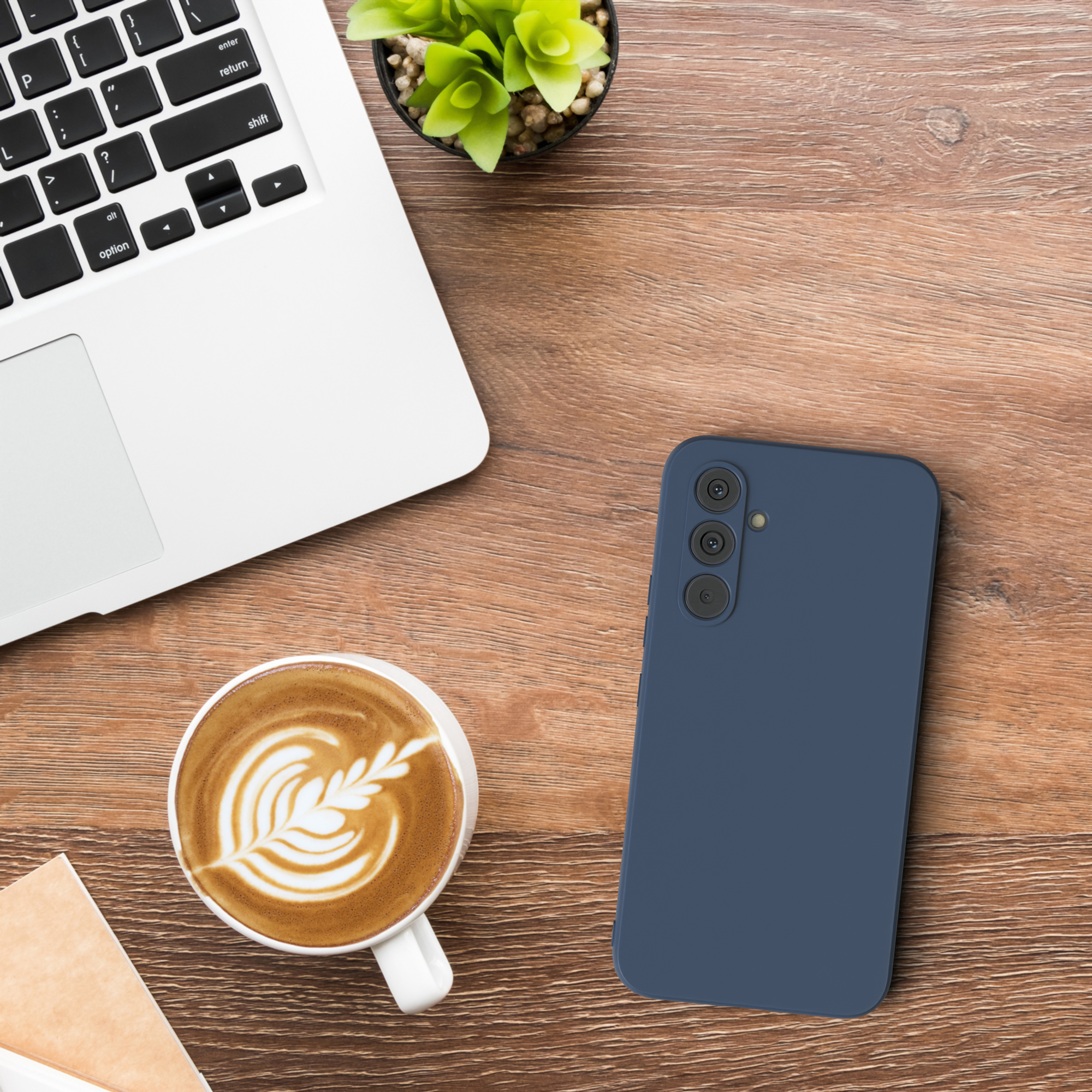 Eine blaue Handyhülle neben einem Laptop und einer Tasse Kaffee mit Latte Art.