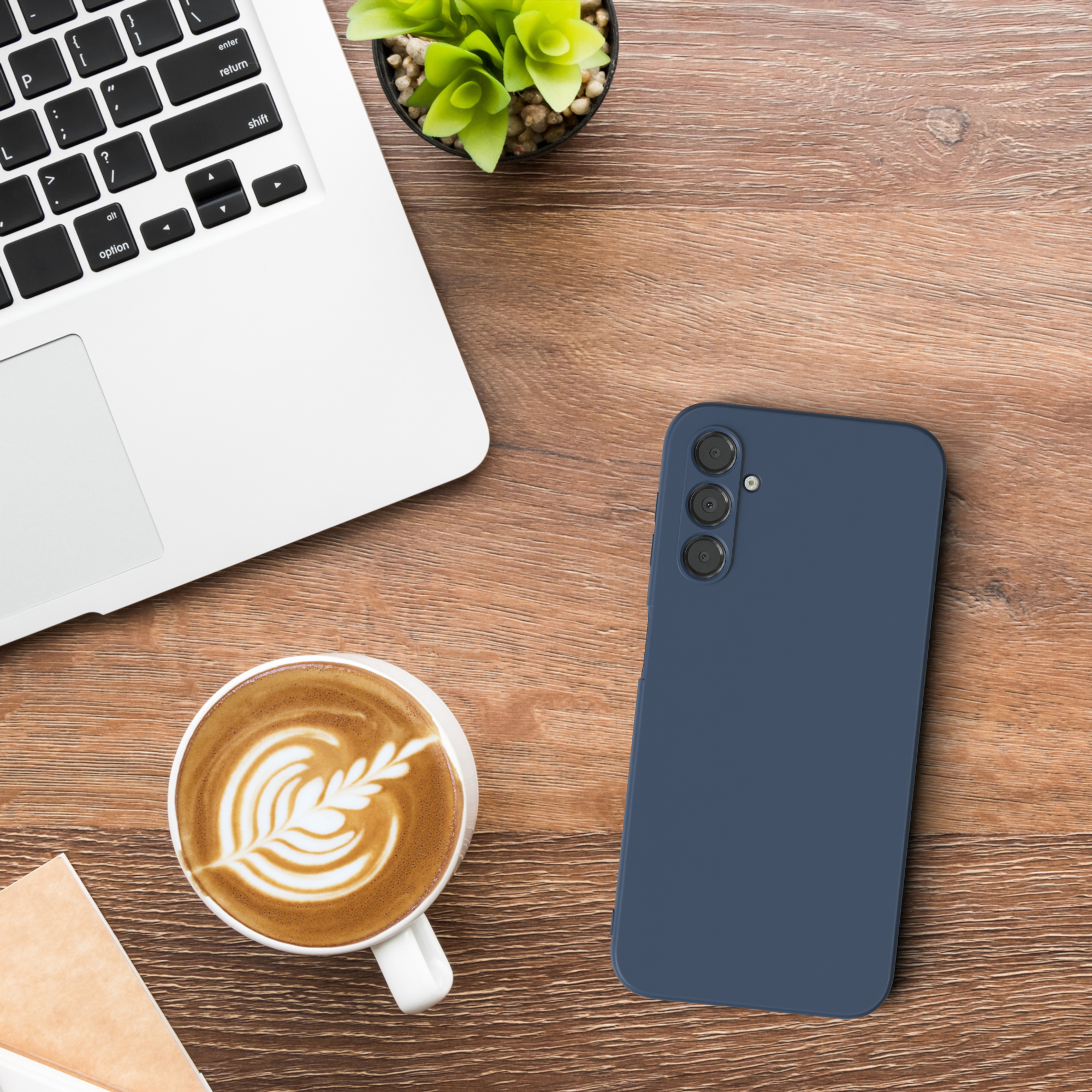 Laptop, Telefon, Kaffeetasse auf einem Holztisch. Eine kleine Pflanze steht neben dem Laptop.