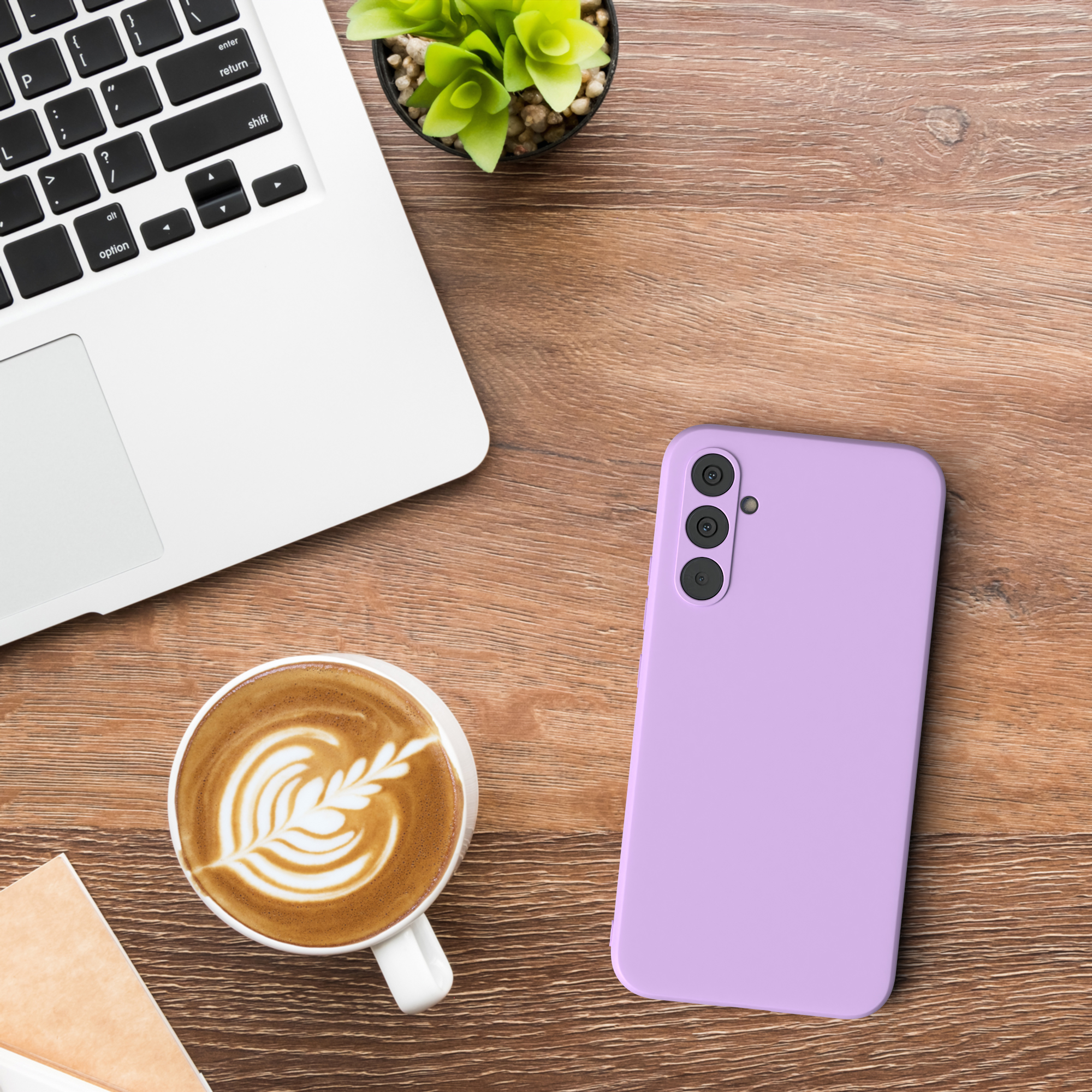 Laptop, Kaffeetasse und eine lilafarbene Handyhülle auf einem Holztisch, mit einer kleinen Pflanze.