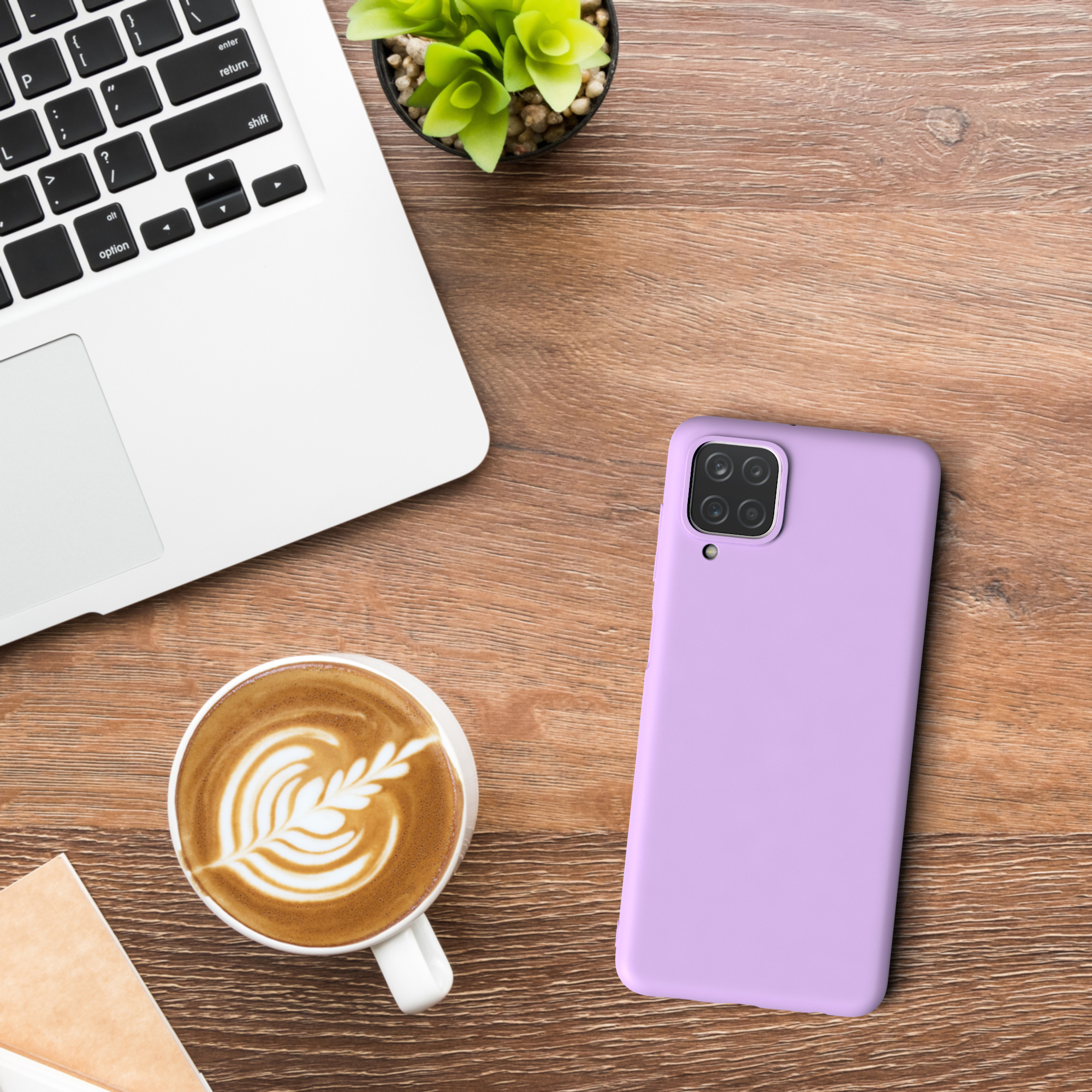 Ein Laptop, eine Kaffeetasse mit Latte Art und eine lila Handyhülle auf einem Holztisch.