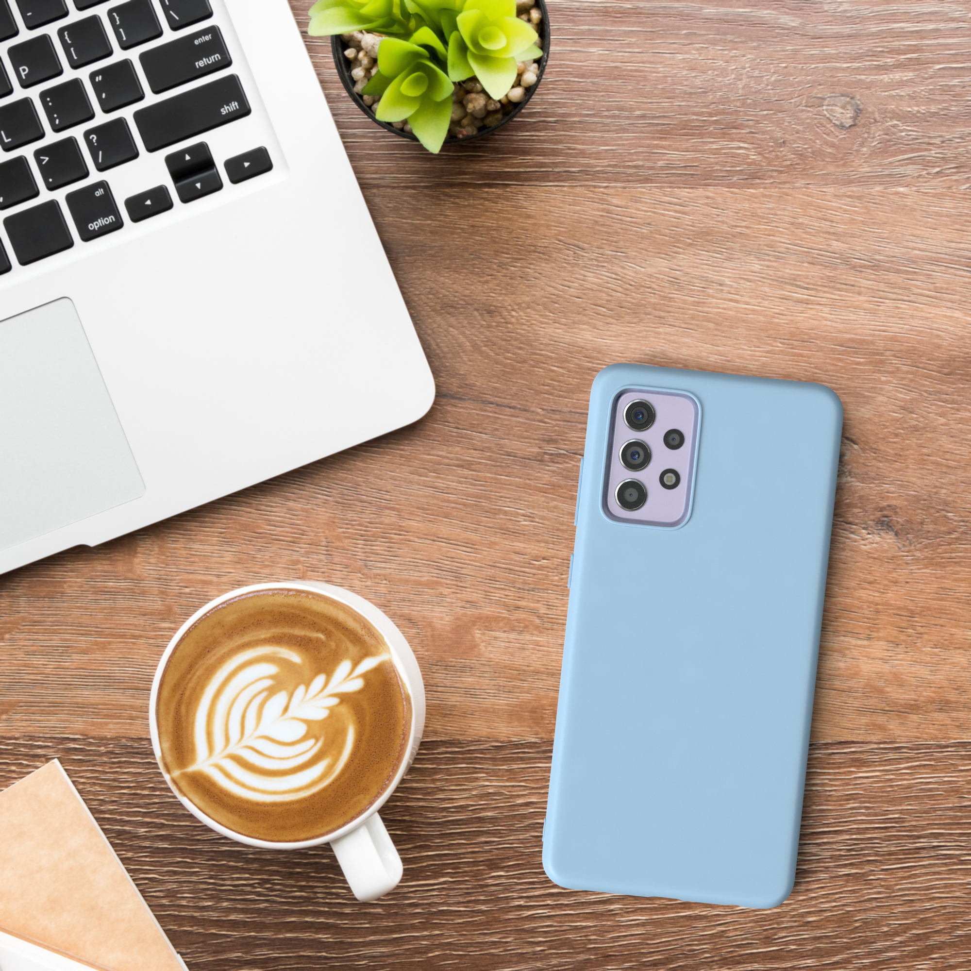 Laptop, Kaffeetasse, Telefon und Pflanze auf einem Holztisch. Der Kaffee hat Latte Art.