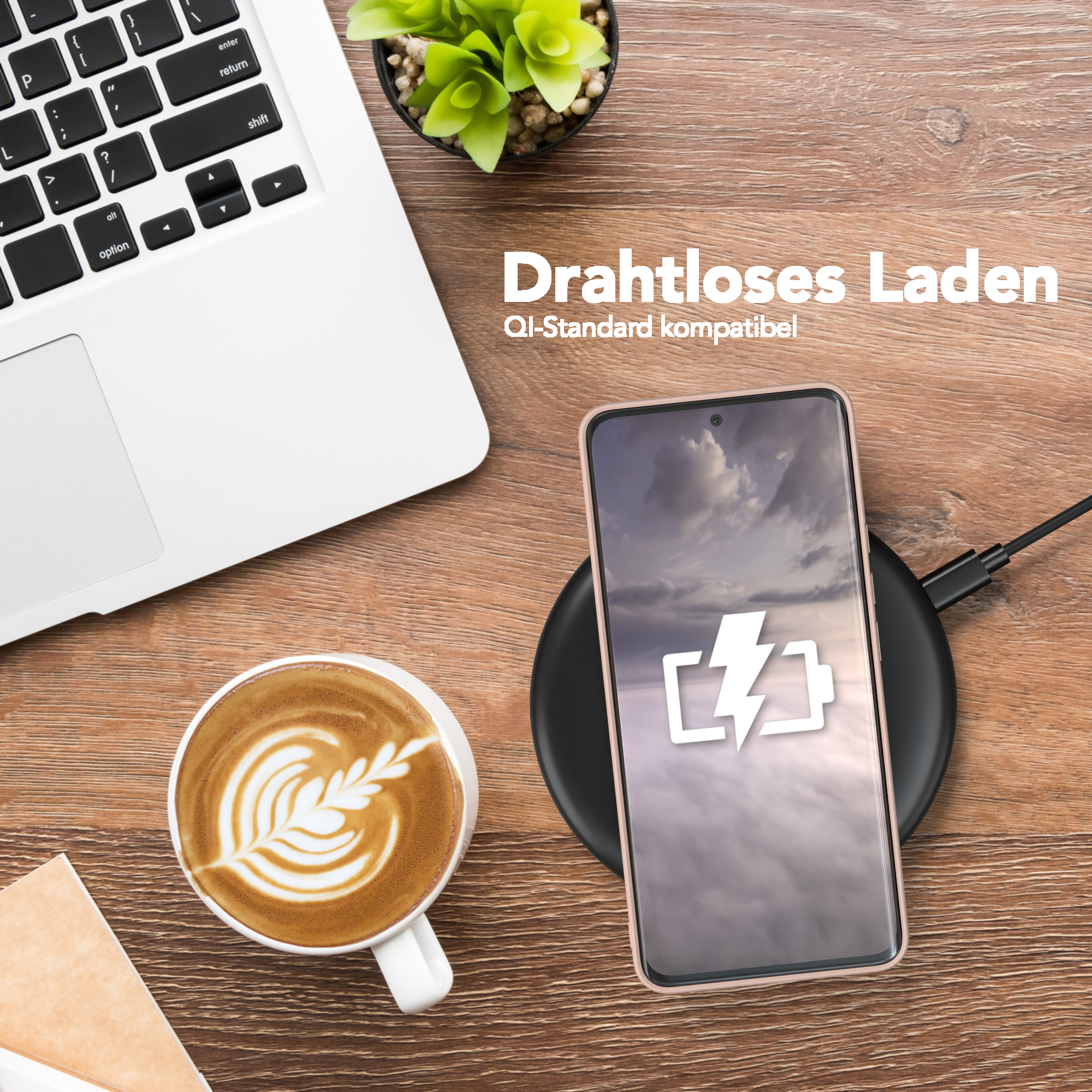 Telefon wird drahtlos auf einem Pad aufgeladen, neben einem Laptop und einer Kaffeetasse mit Latte Art.