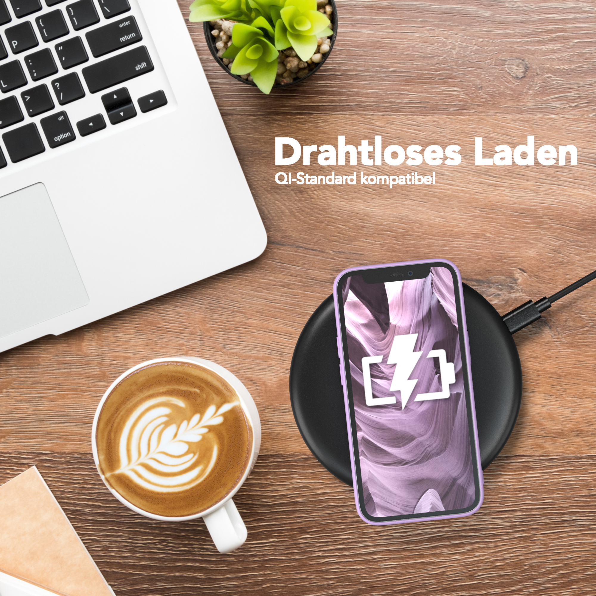 Laptop, Kaffee mit Kunst, Telefon lädt auf Pad, kleine Pflanze auf Holztisch.
