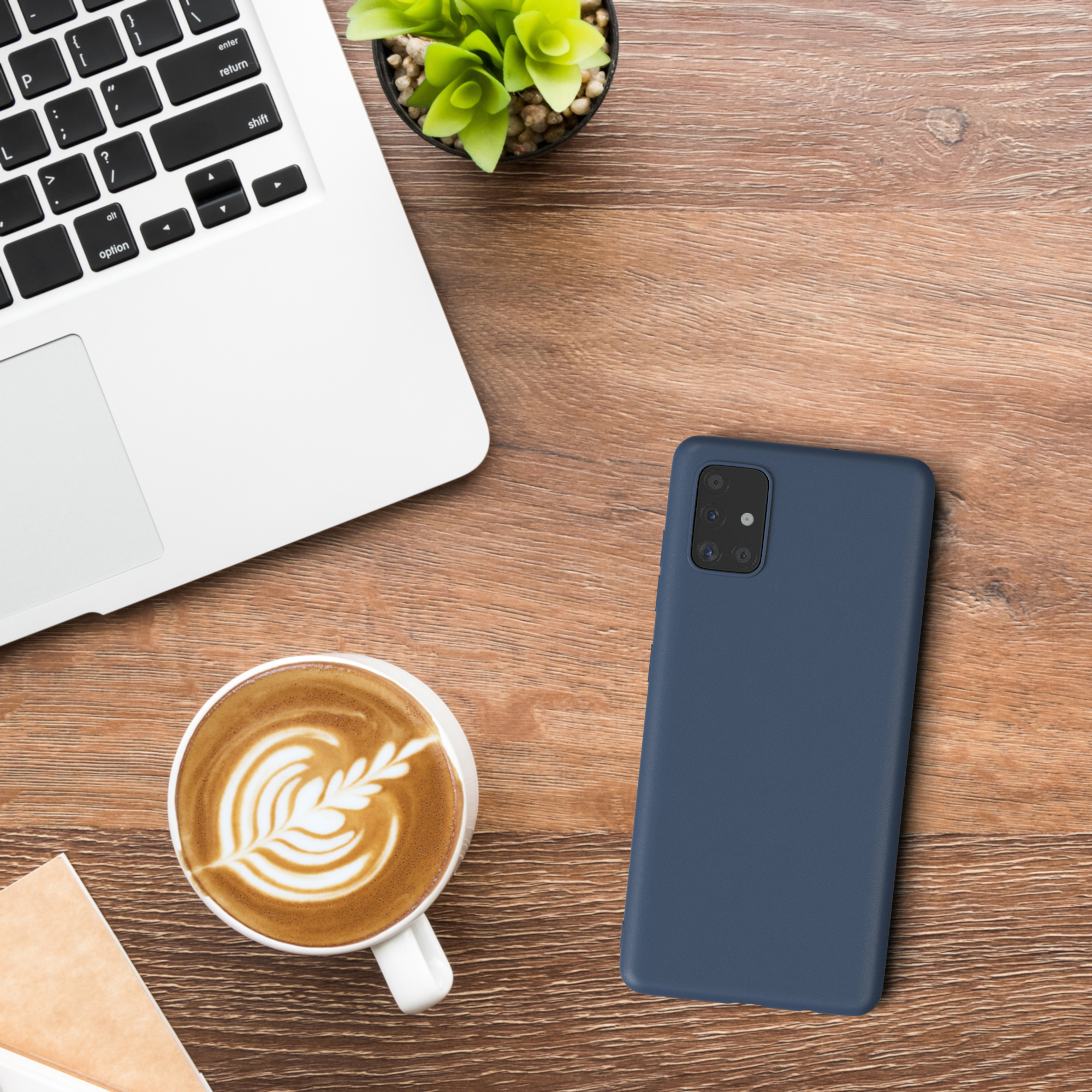 Telefon auf einem Holztisch, neben einem Laptop und einer Tasse Kaffee. Pflanze im Hintergrund.