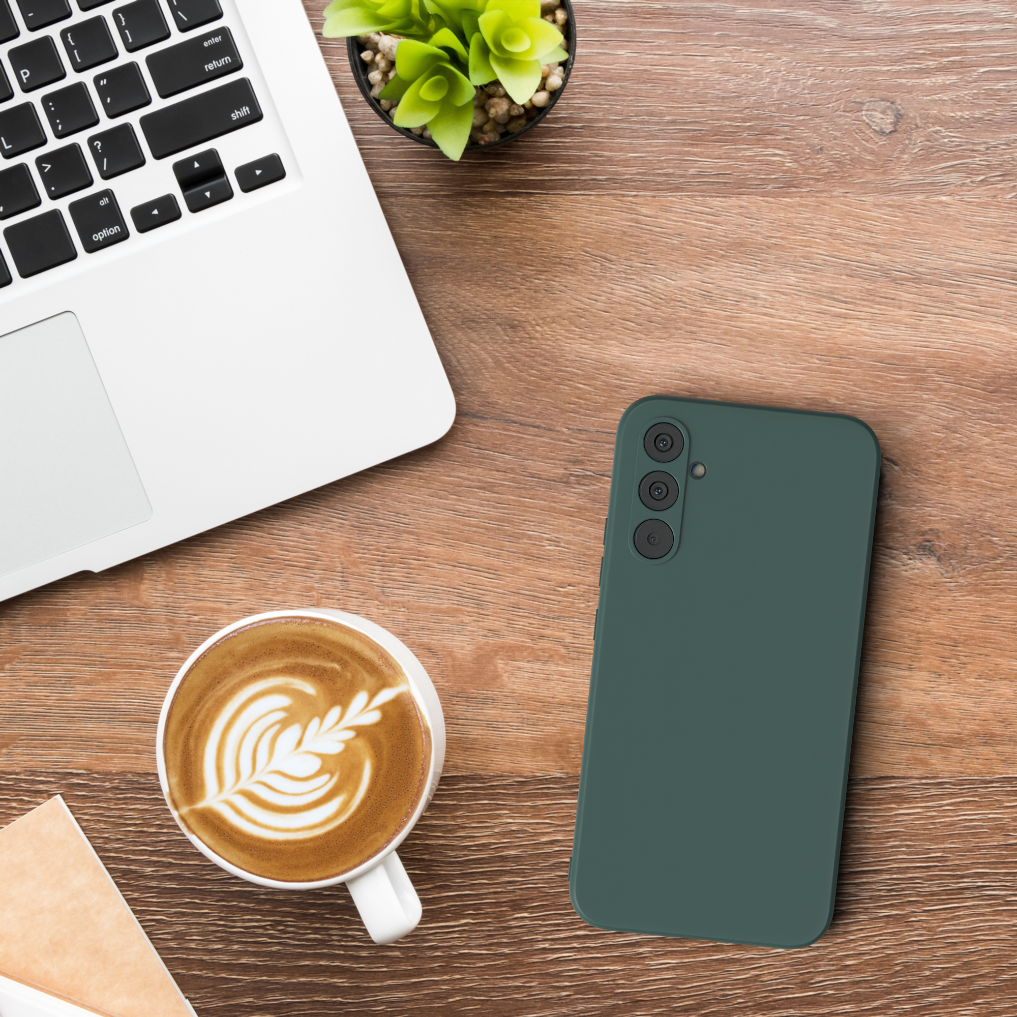 Laptop, Telefon, Kaffee auf Holztisch. Telefon ist grün. Kaffee hat Latte Art. Pflanze im Hintergrund.