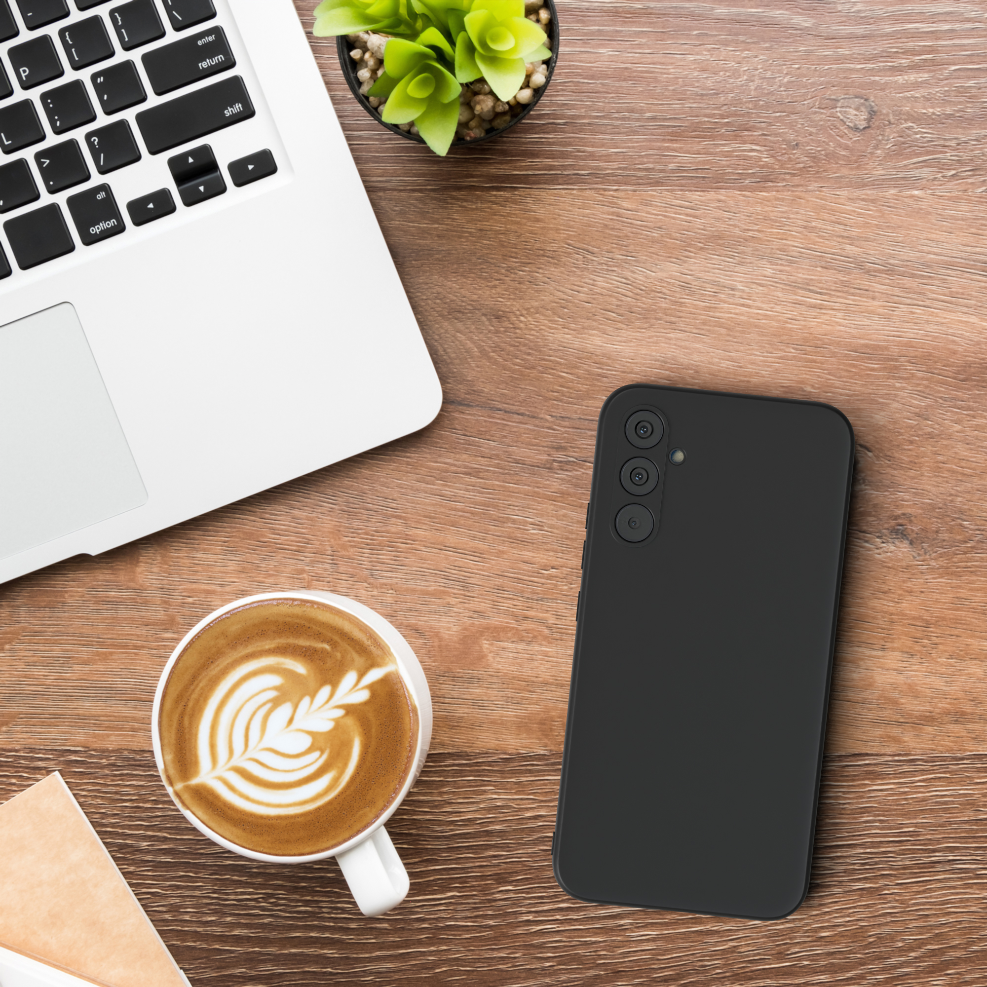 Ein Laptop, eine Kaffeetasse mit Design und eine schwarze Handyhülle mit drei Kameralinsen.