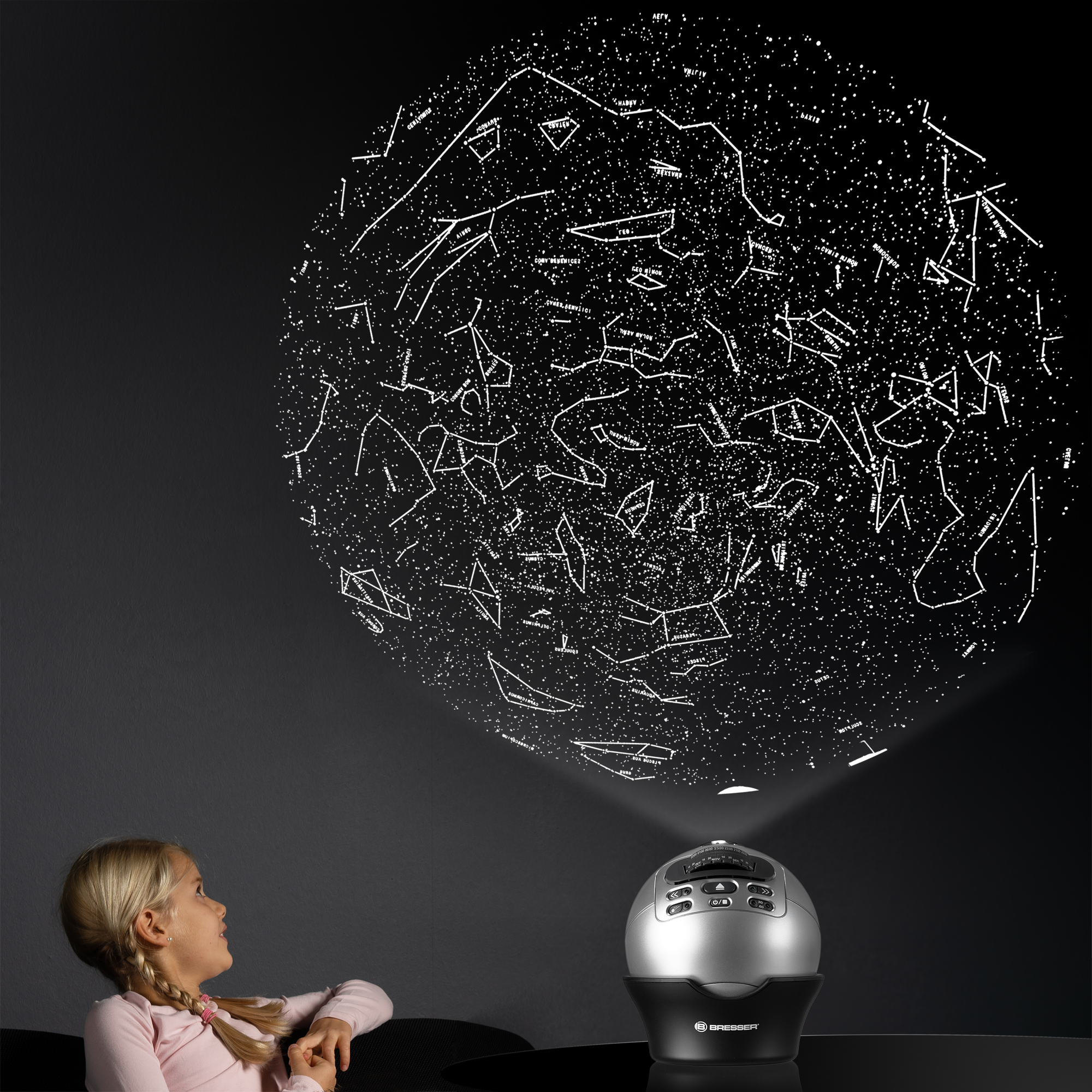 Niña mirando un proyector de planetario que proyecta estrellas en una pared oscura.