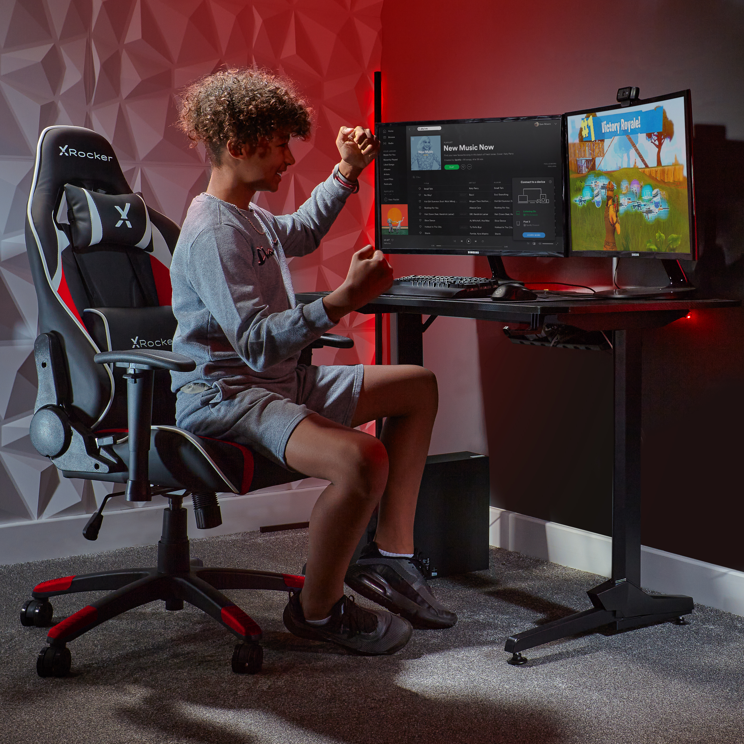 Junger Mann sitzt in einem Gaming-Stuhl und spielt ein Spiel auf zwei Monitoren. Rotes und schwarzes Setup.