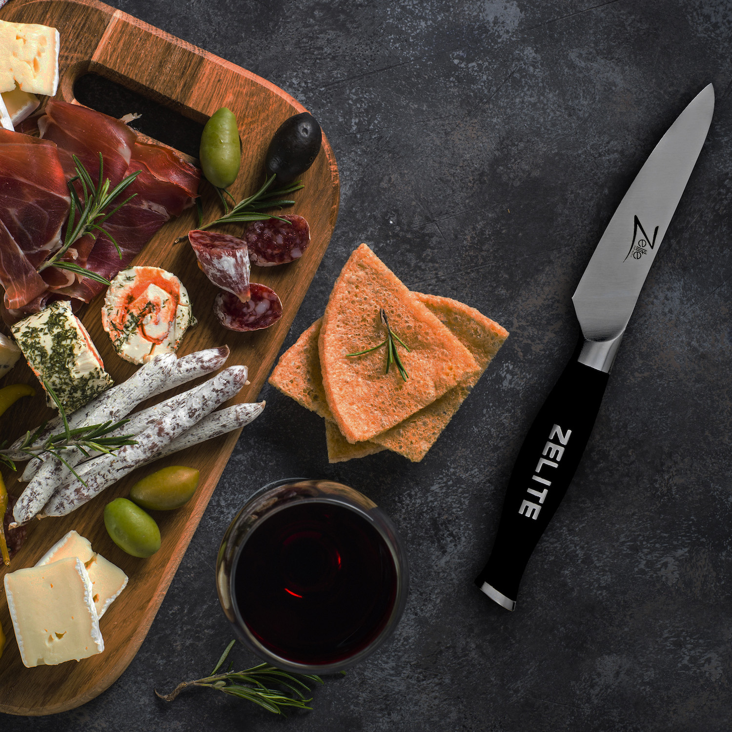 Ein Holzbrett mit Käse, Fleisch, Crackern, Oliven und einem Glas Rotwein. Ein Messer liegt daneben.