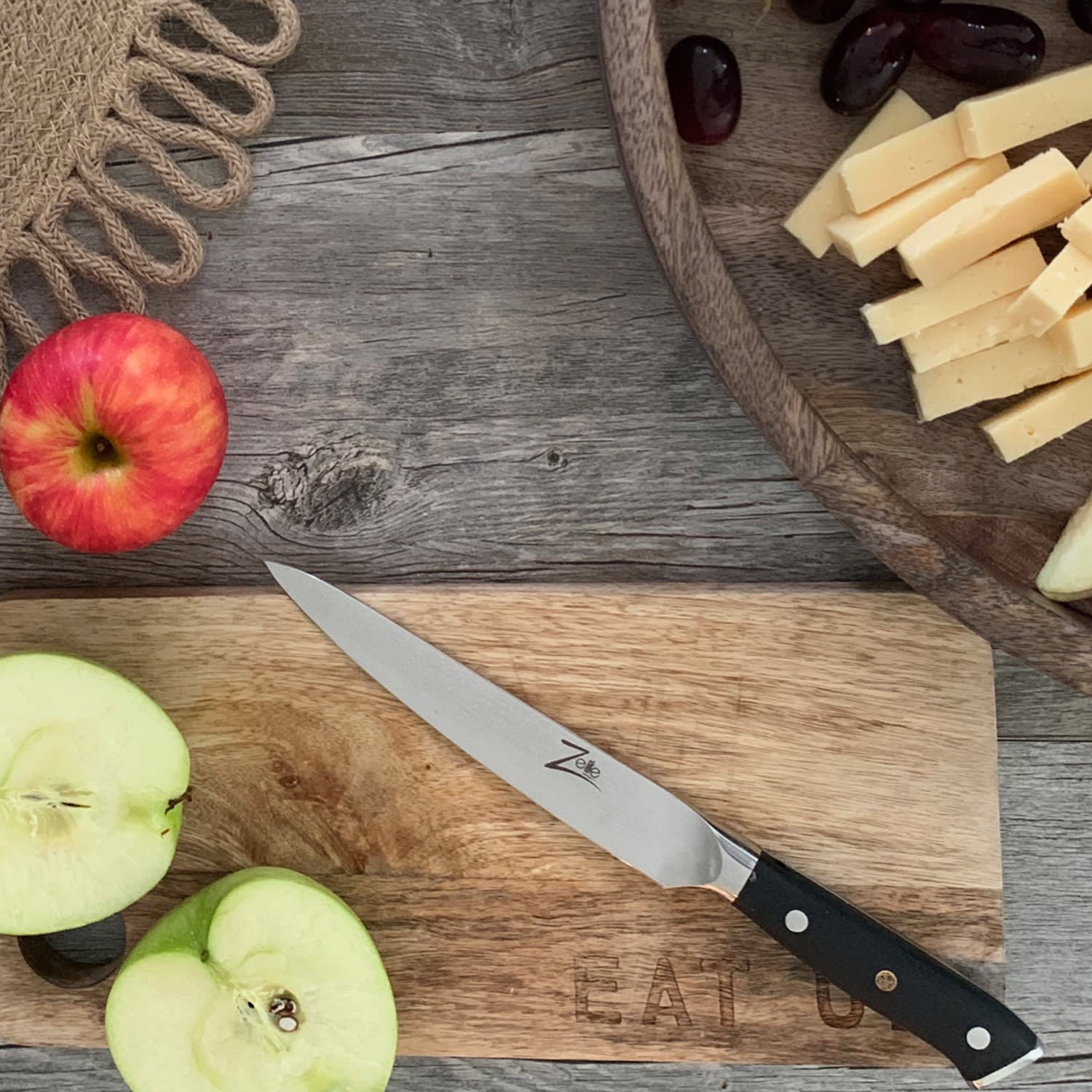 Holztisch mit Messer, Käse, Trauben und geschnittenem Apfel.