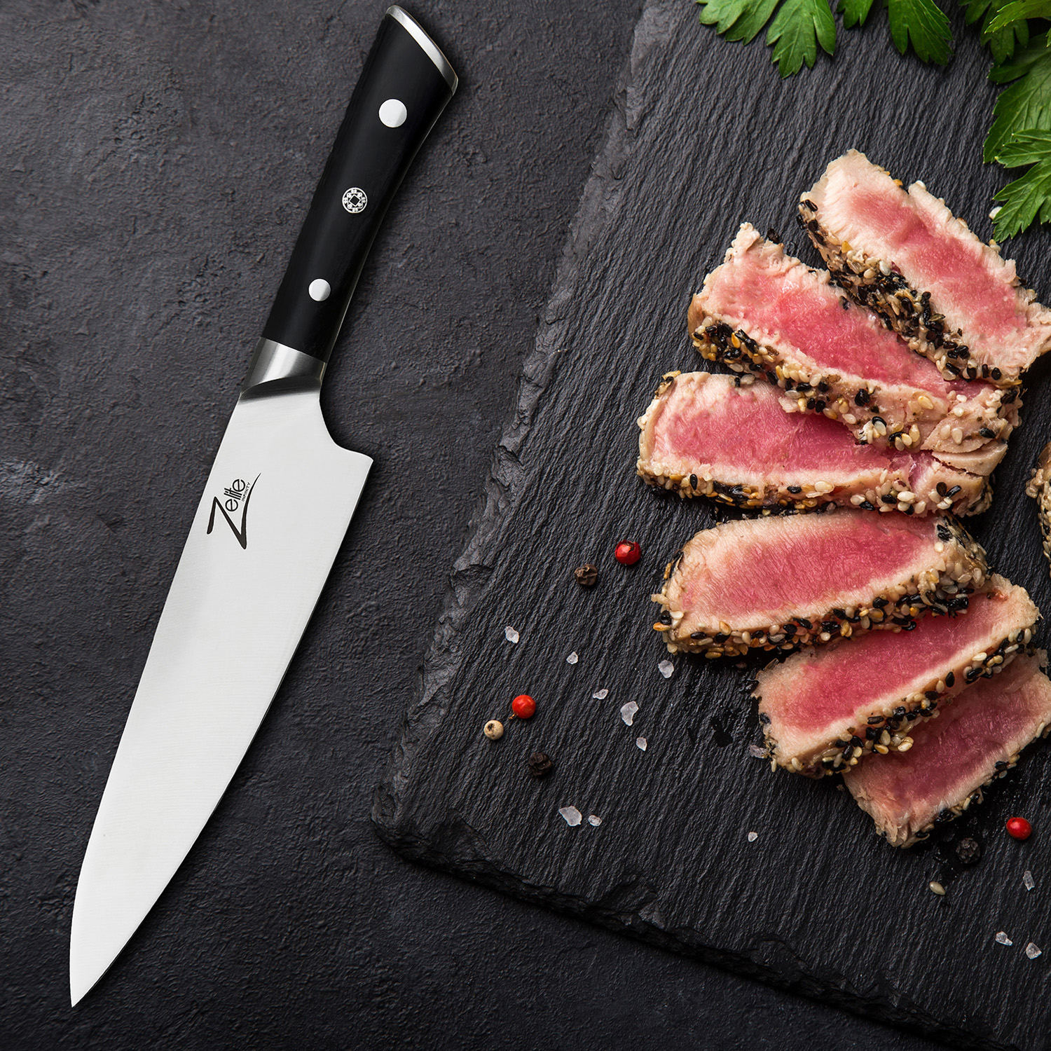 Ein Kochmesser neben geschnittenen Thunfischsteaks auf einem schwarzen Schneidebrett. Rote und schwarze Pfefferkörner.