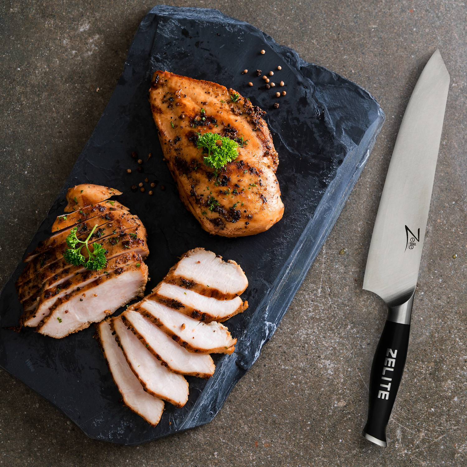 Gegrillte Hähnchenbrust mit Scheiben und Messer auf Schieferplatte.